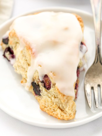 A closeup shot of a lemon blueberry scone on a white plate with a fork on the side.