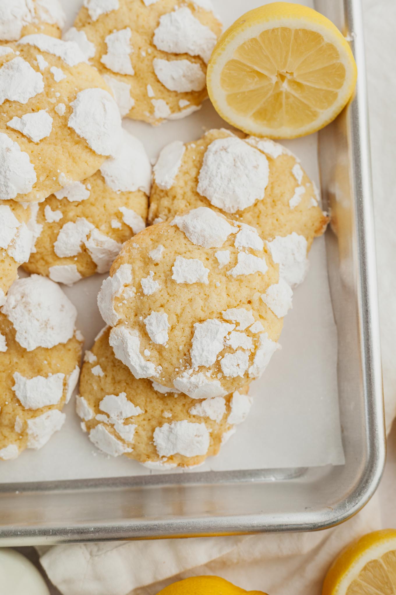 An overhead view of lemon crinkle cookies on a parchment paper-lined baking tray.