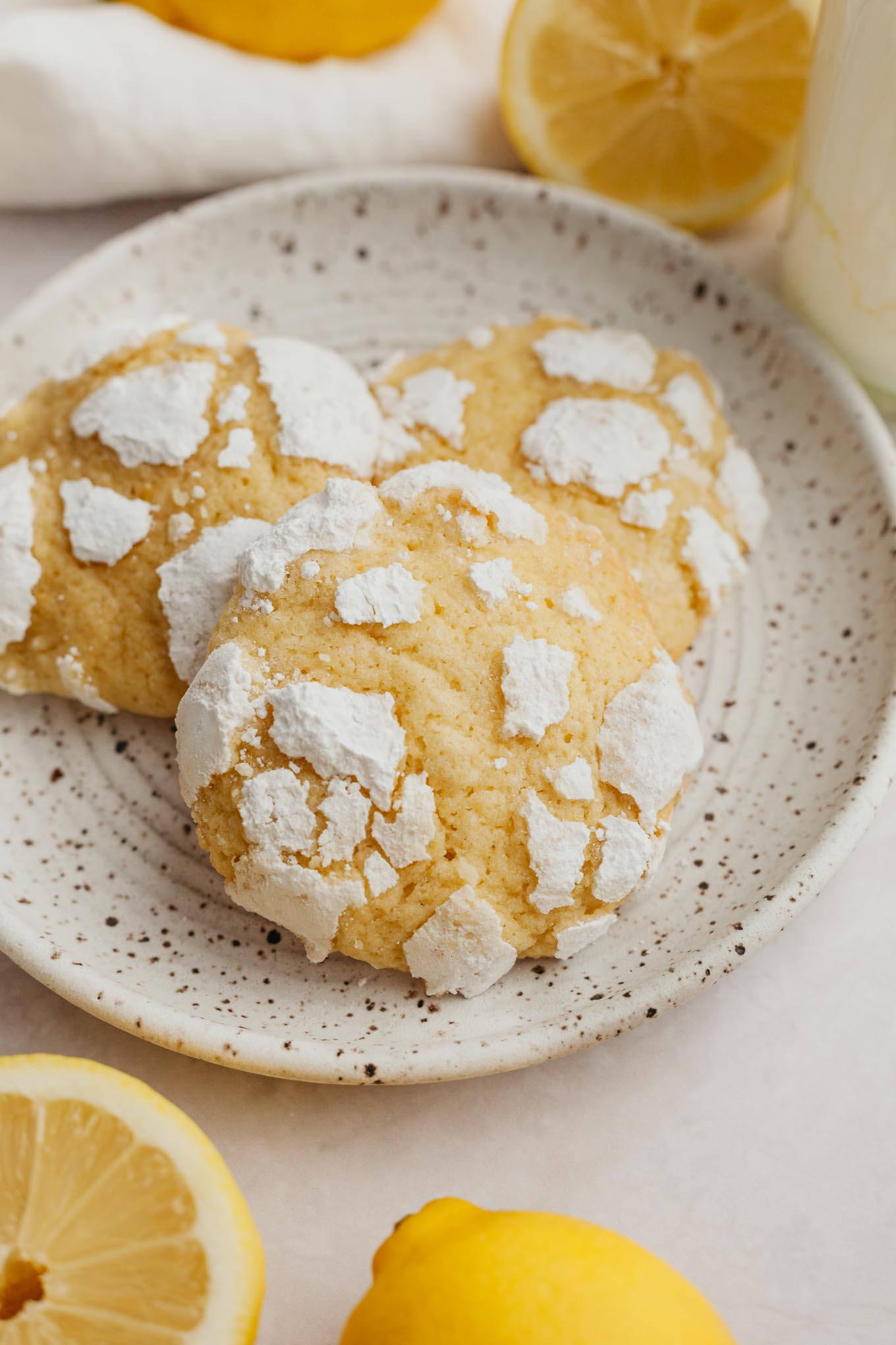 Three lemon crinkles on a speckled white dessert plate. 