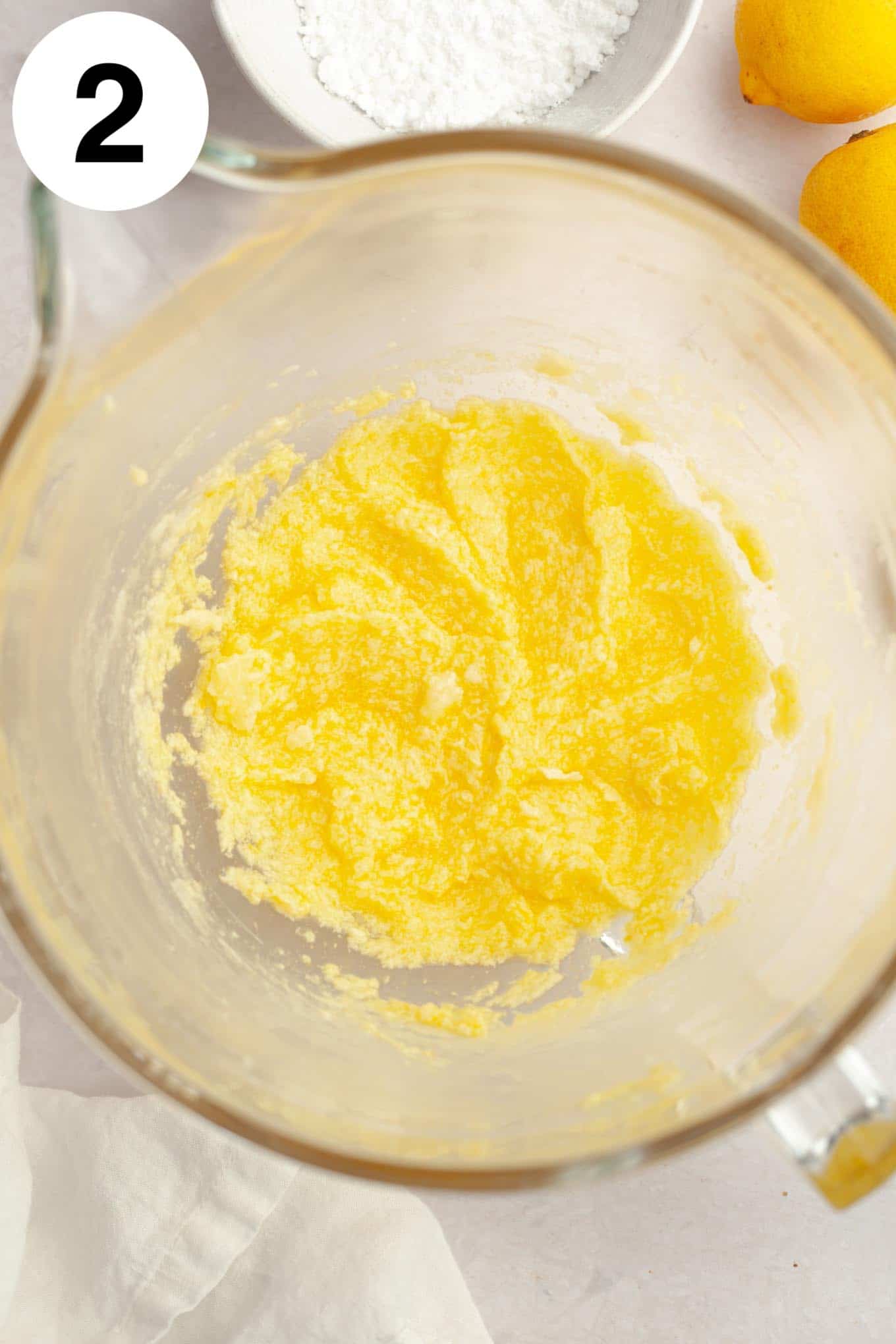 An overhead view of creamed butter, sugar, egg, and lemon in a glass mixing bowl. 