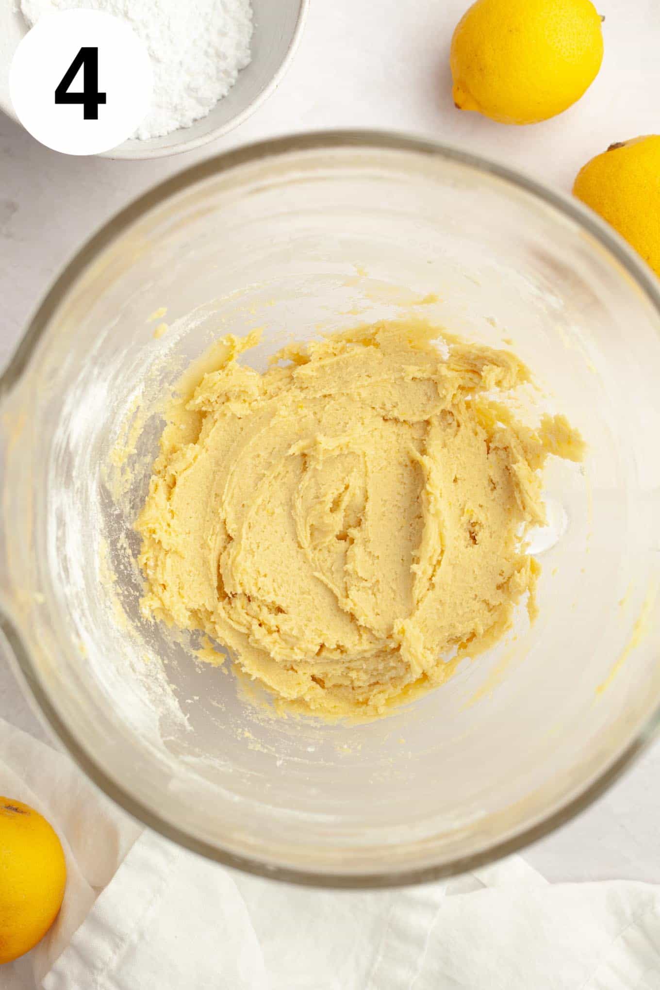 An overhead view of lemon cookie dough in a glass mixing bowl. 