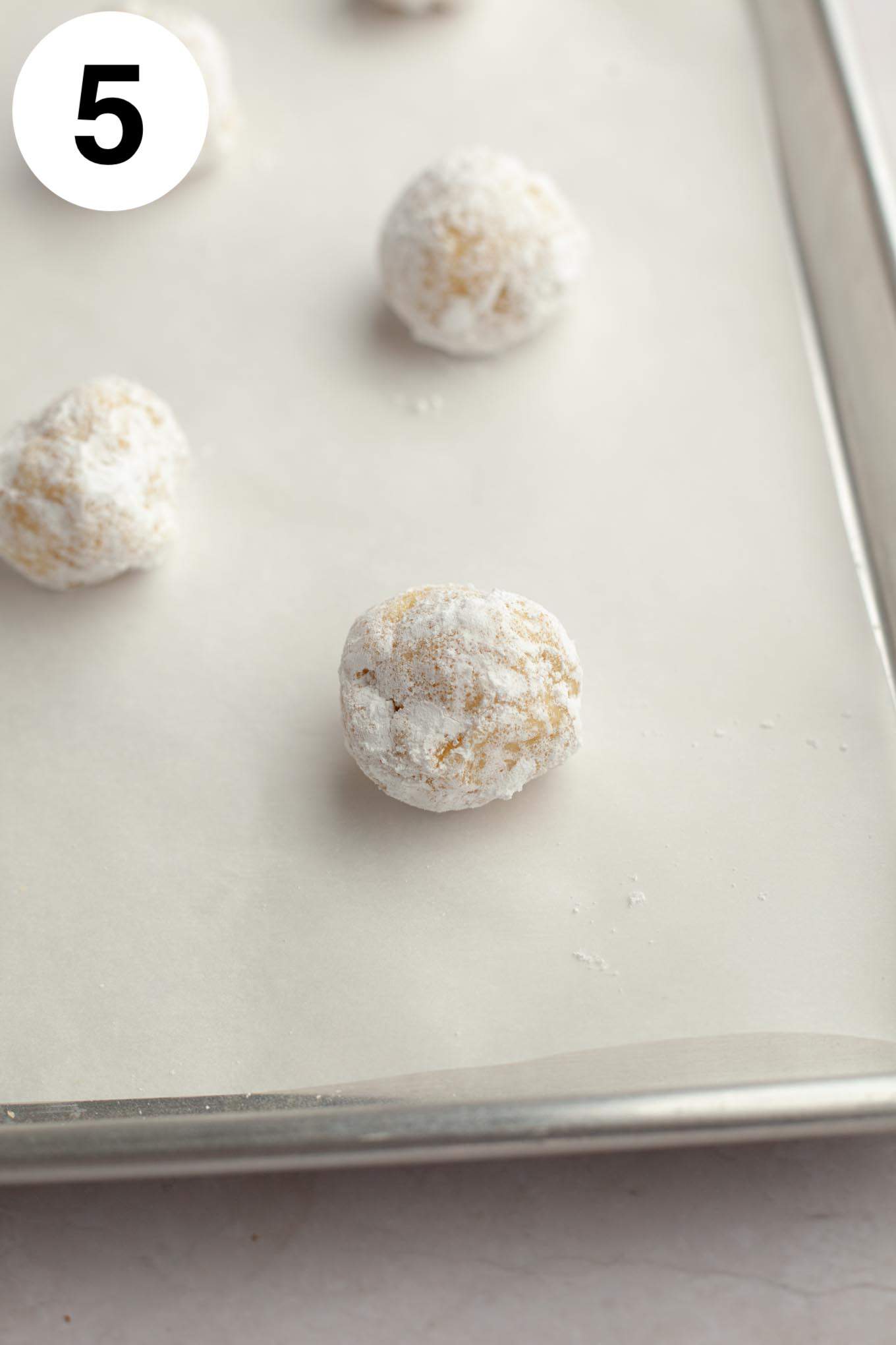 Raw lemon crinkle cookie dough balls on a parchment paper-lined baking sheet. 