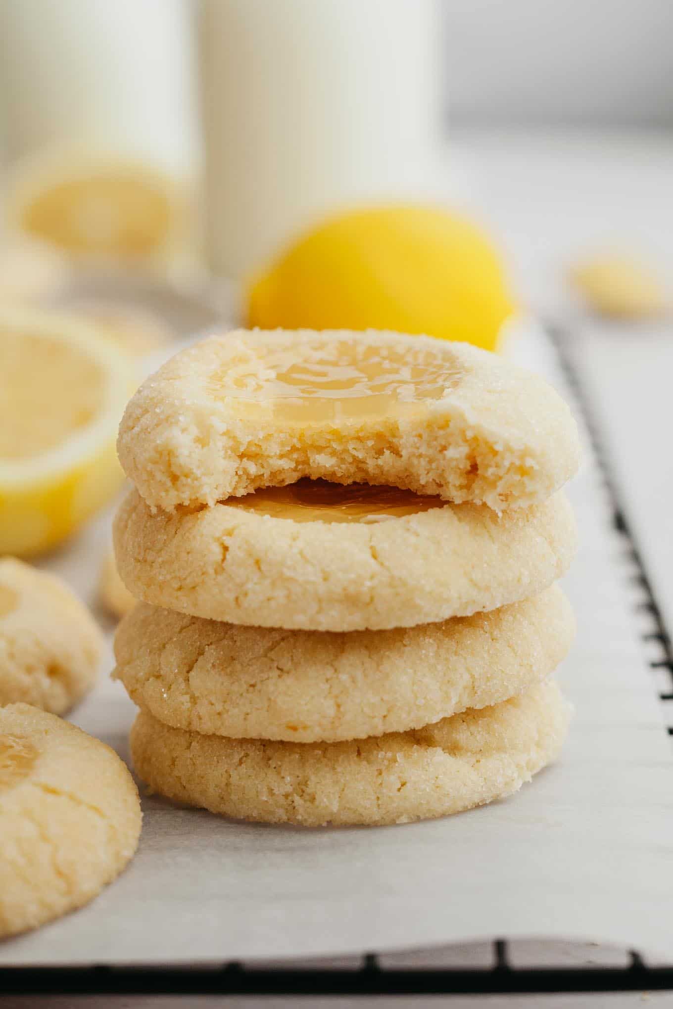 A stack of four lemon curd thumbprints. The top cookie has a bite missing. 