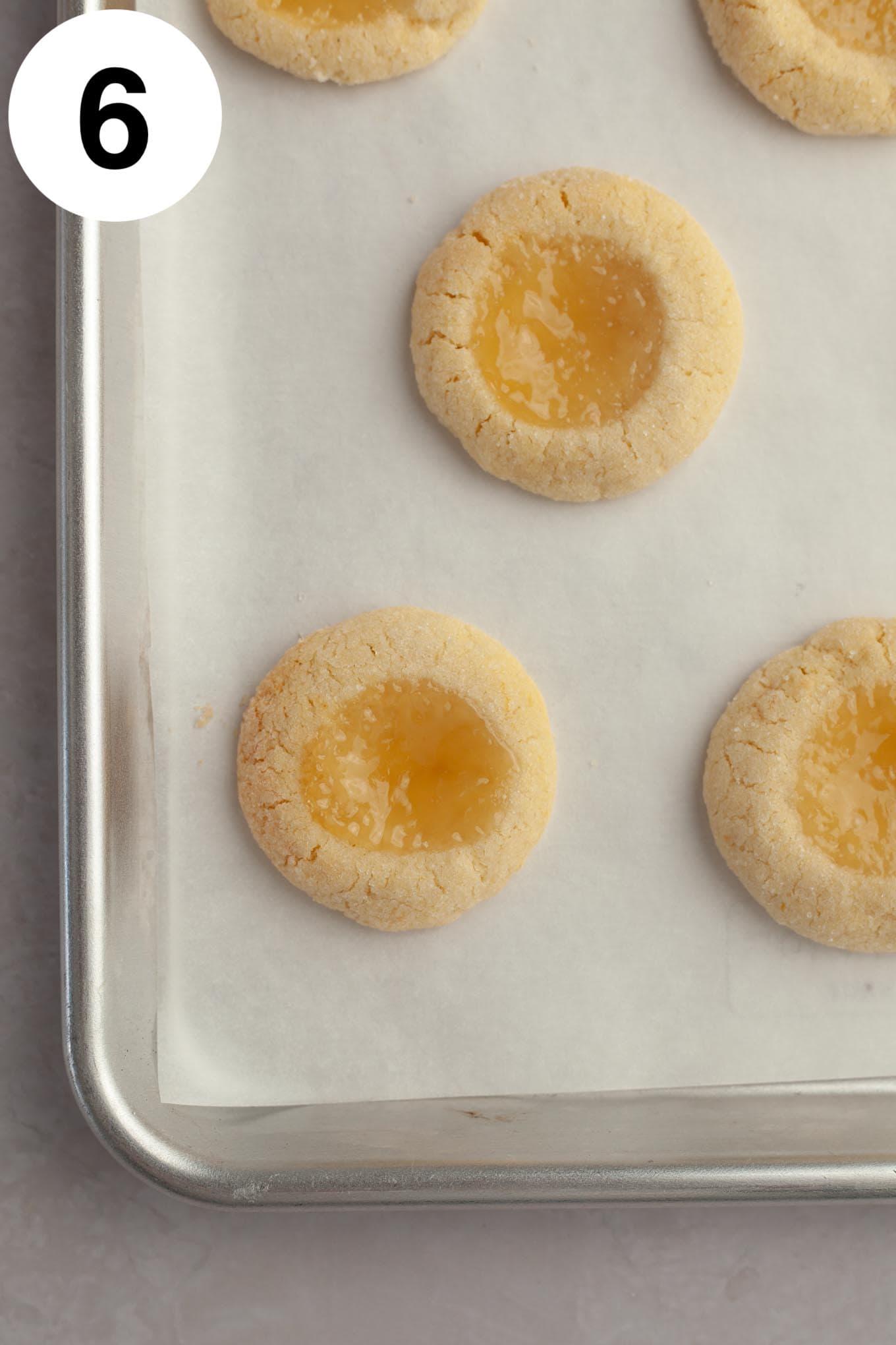 An overhead view of baked lemon curd cookies on a parchment-lined baking sheet. 