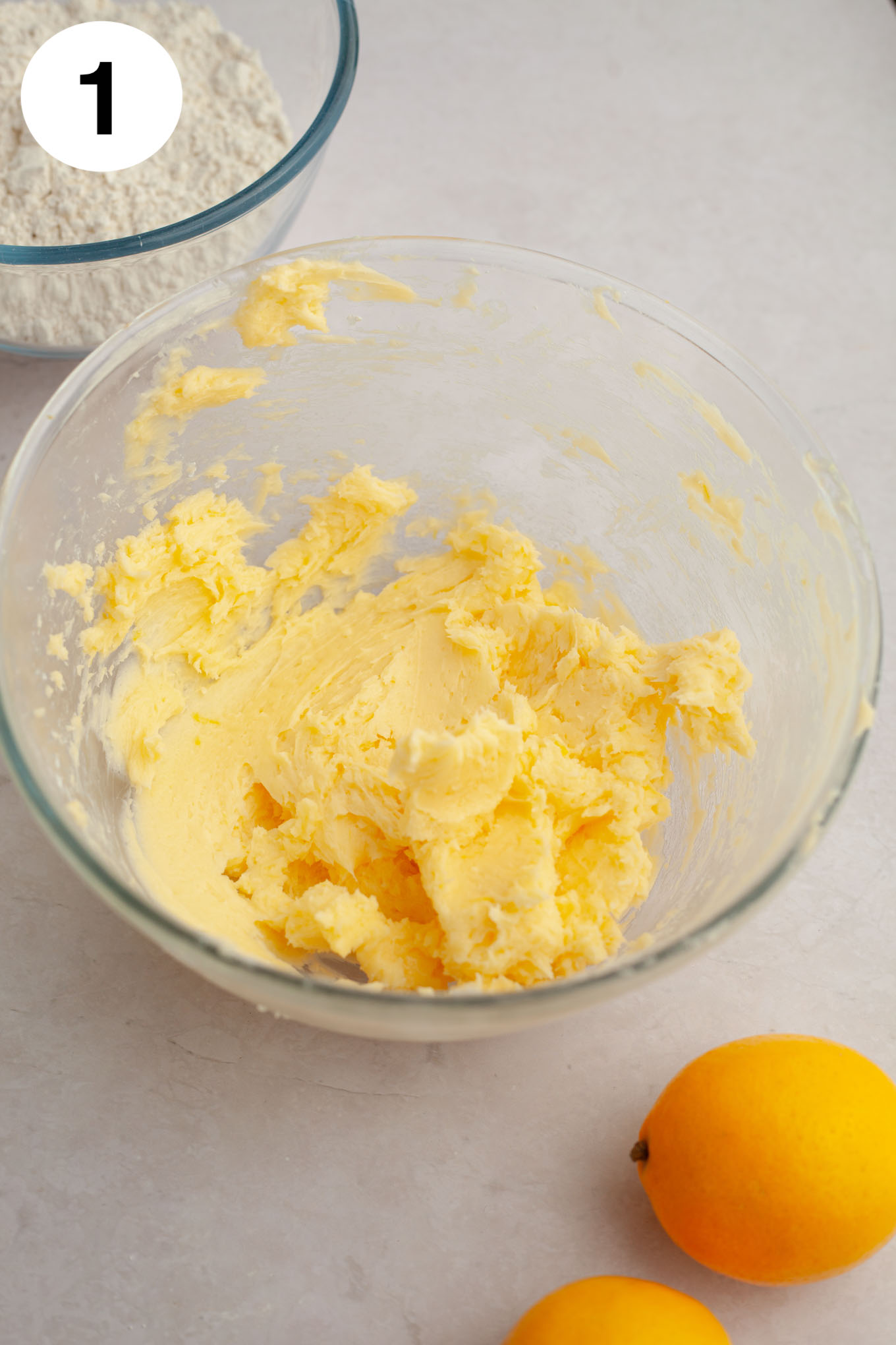 An overhead view of creamed butter, sugar, egg, and lemon in a glass mixing bowl.