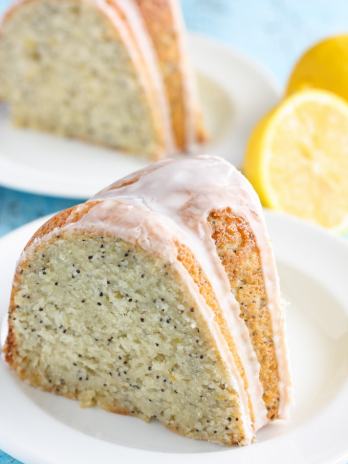 Two slices of glazed lemon poppy seed bundt cake on white plates.