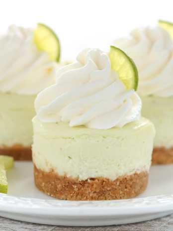 Three mini key lime cheesecakes topped with whipped cream and key lime wedges on a white plate.