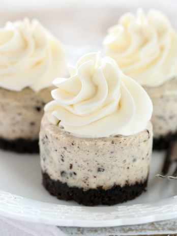 Three mini Oreo cheesecakes topped with whipped cream sitting on a white plate.