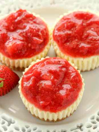 Three mini strawberry cheesecakes on a decorative white plate.
