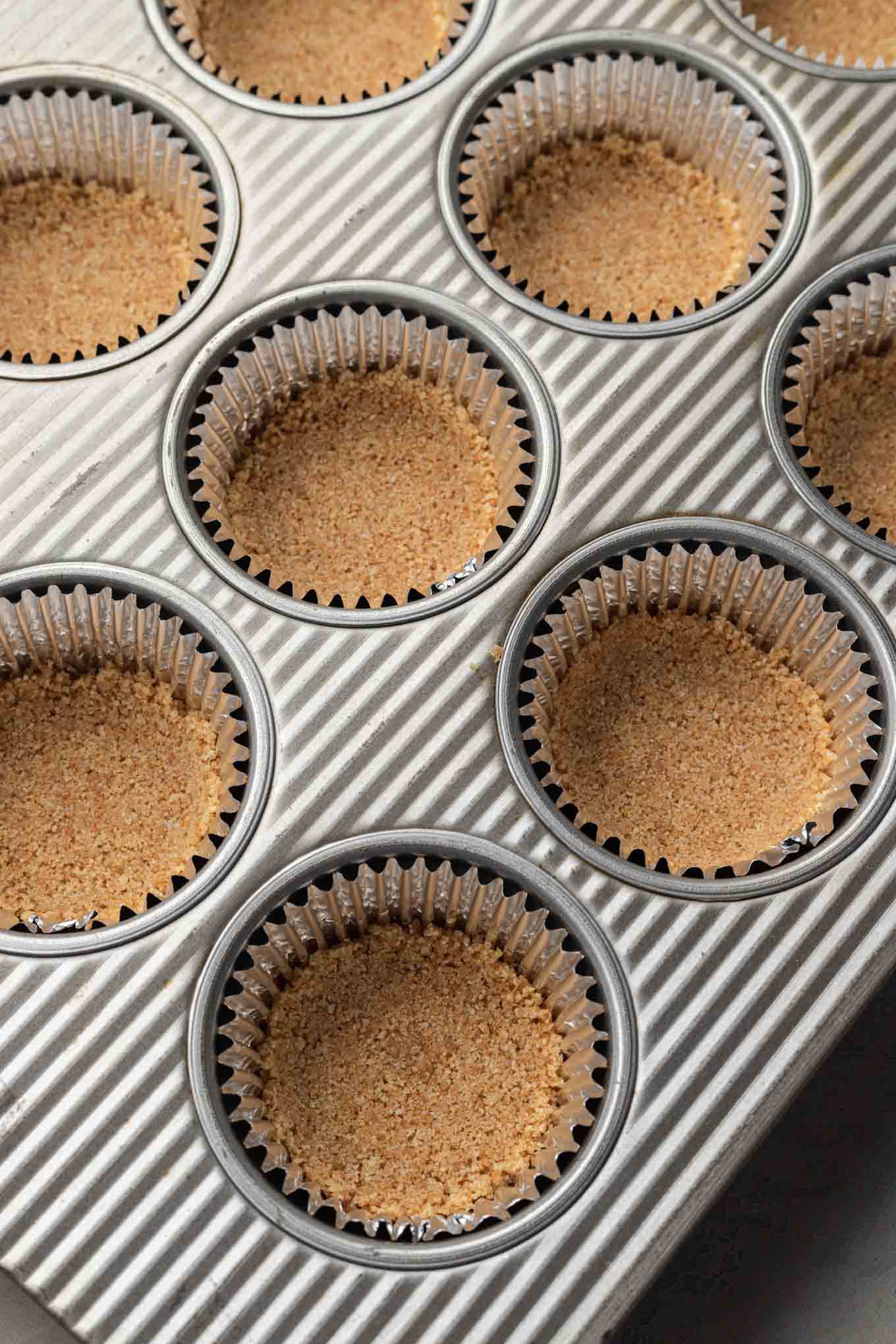 Muffin cups lined with cupcake liners and filled with a graham cracker crust. 