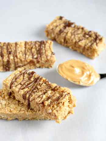 Four no bake peanut butter granola bars drizzled with chocolate. A spoonful of peanut butter rests nearby.