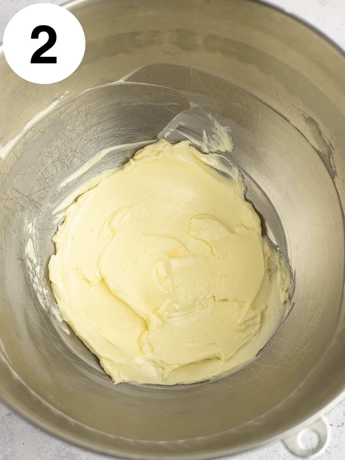 An overhead view of beaten butter in a metal mixing bowl. 