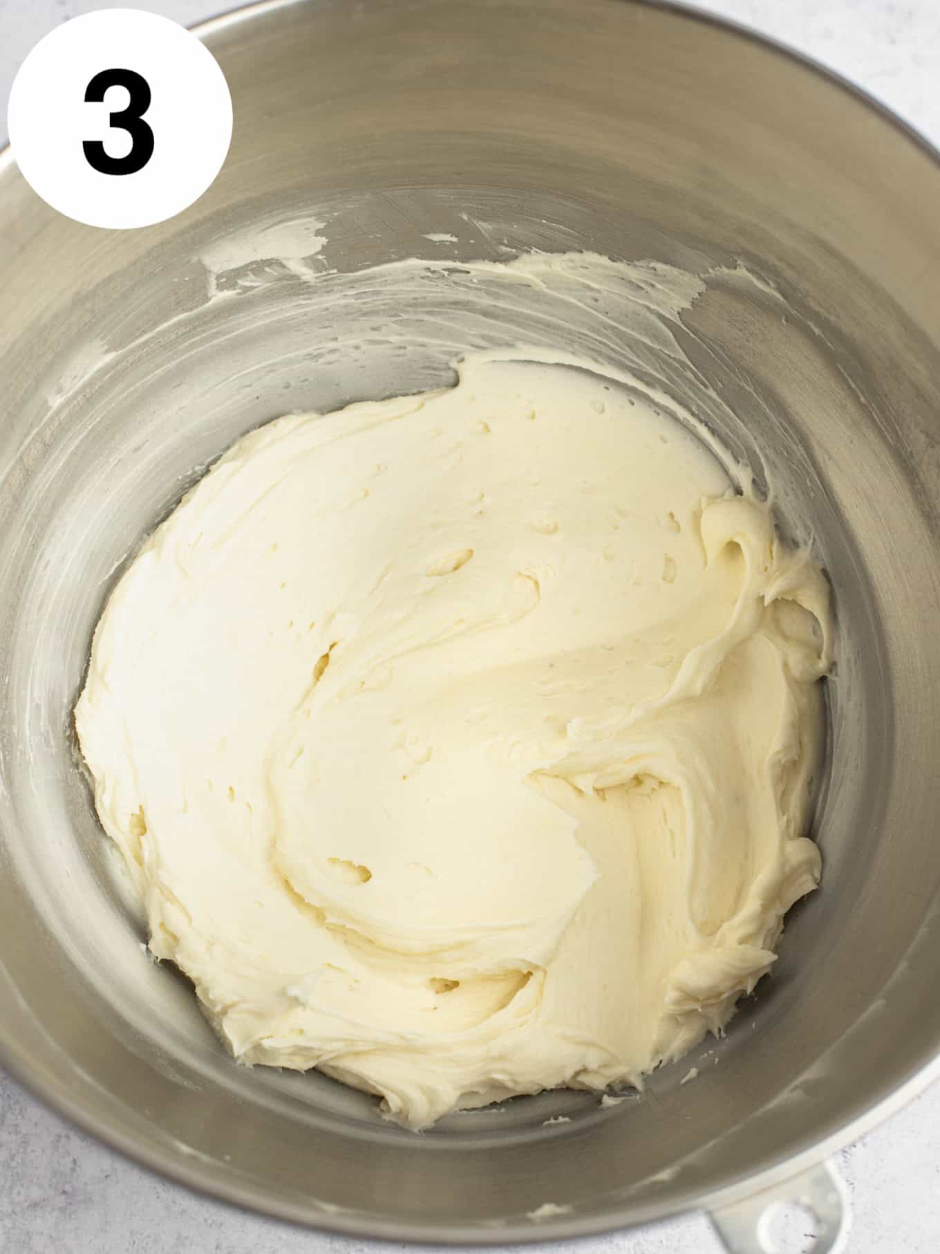 An overhead view of buttercream in a metal mixing bowl. 