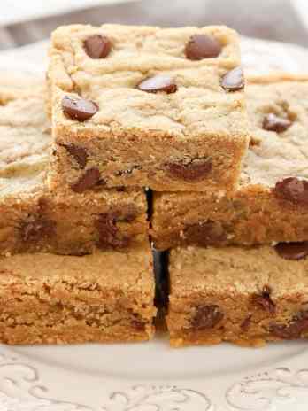 Five peanut butter chocolate chip bars stacked on a white plate.