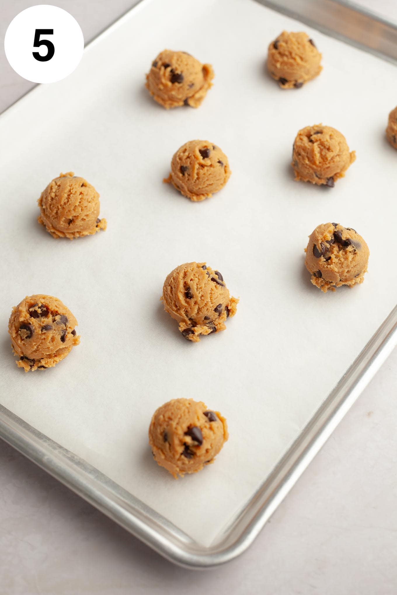 Balls of peanut butter chocolate chip cookie dough on a parchment-lined baking sheet. 
