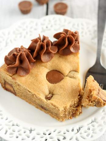 A slice of homemade cookie cake on a white plate with a fork.