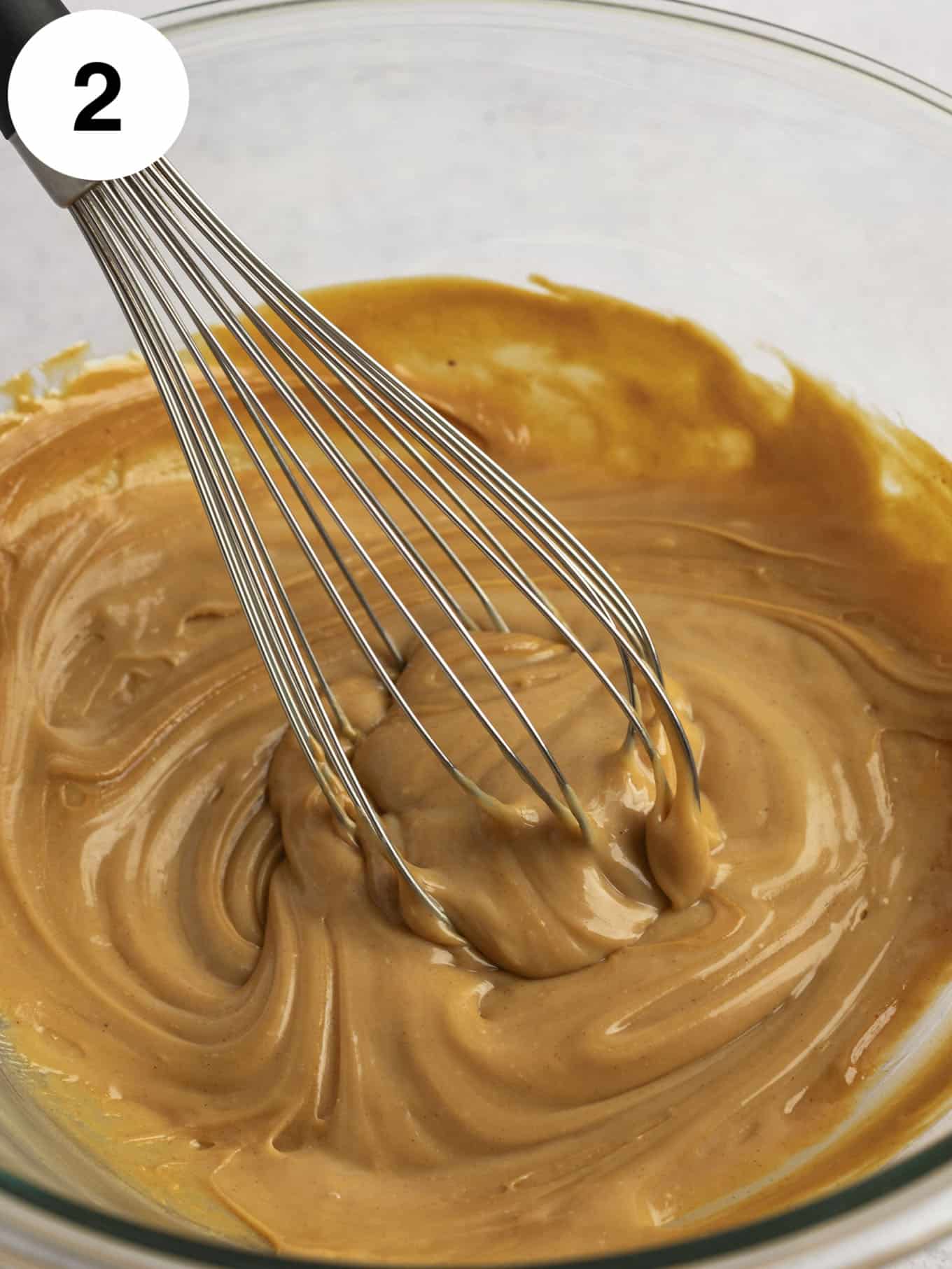A peanut butter and sweetened condensed milk mixture in a glass mixing bowl, with a whisk. 