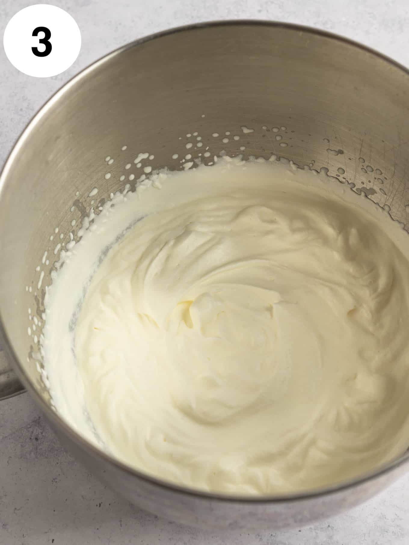 An overhead view of whipped cream in the bowl of a stand mixer. 