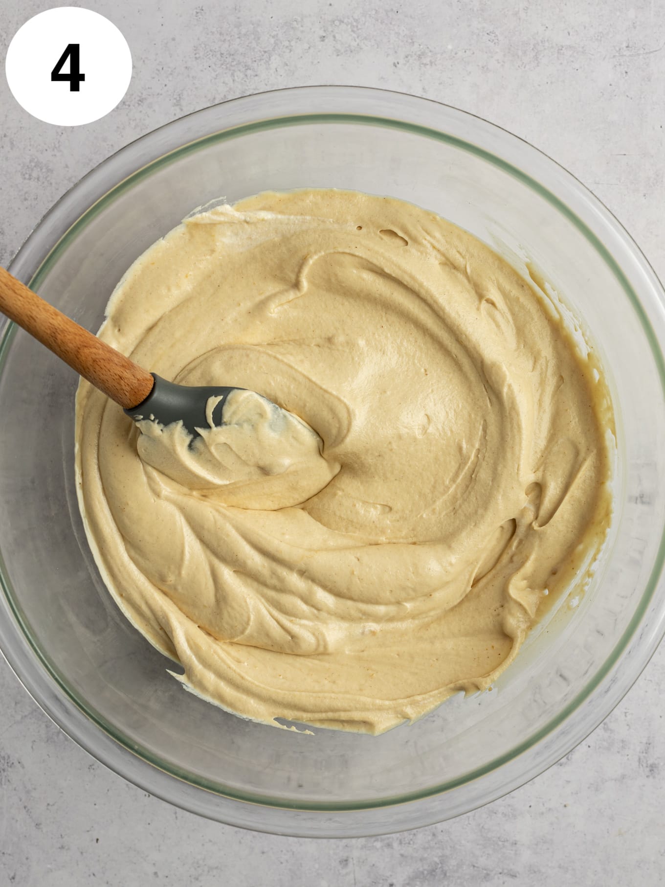 An overhead view of a peanut butter ice cream base in a glass mixing bowl, with a rubber spatula. 