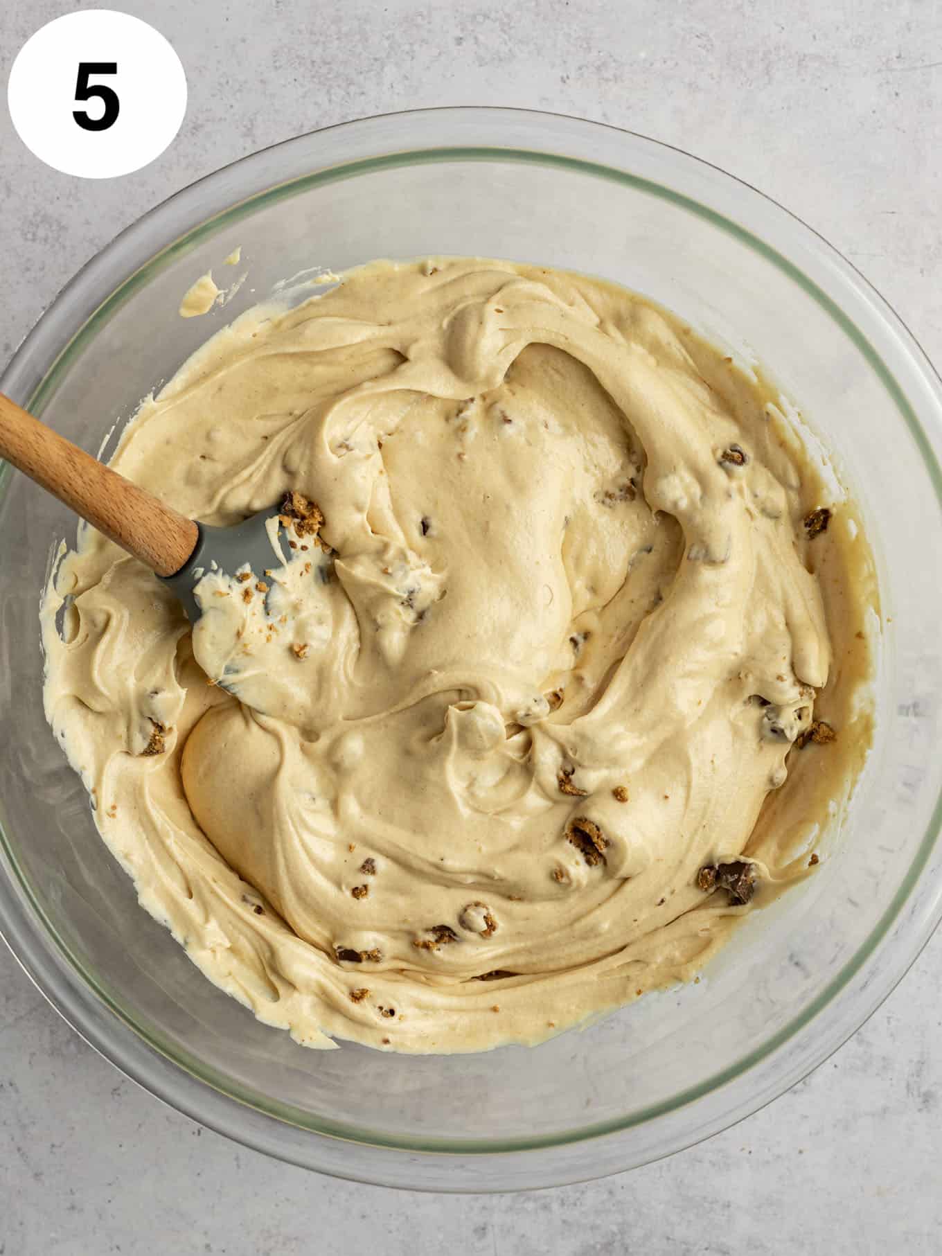 An overhead view of a peanut butter cup ice cream base in a glass mixing bowl, with a rubber spatula. 