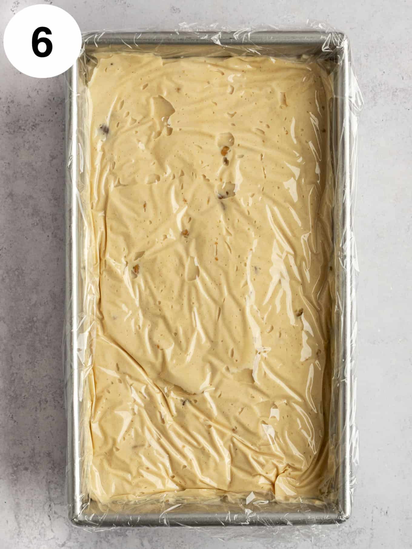 An overhead view of PB ice cream in a loaf pan, with plastic wrap pressed on top. 
