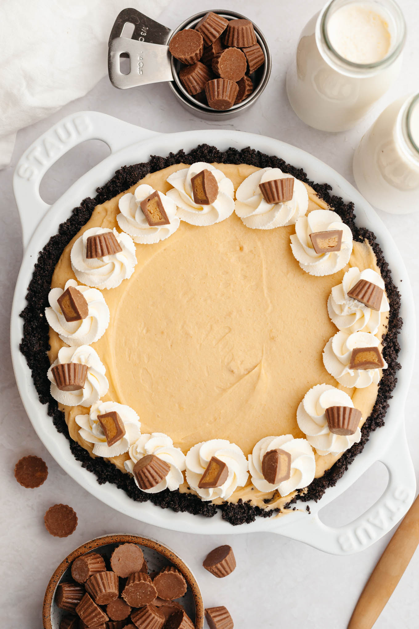 An overhead view of a peanut butter pie decorated with whipped cream and halved mini peanut butter cups. 