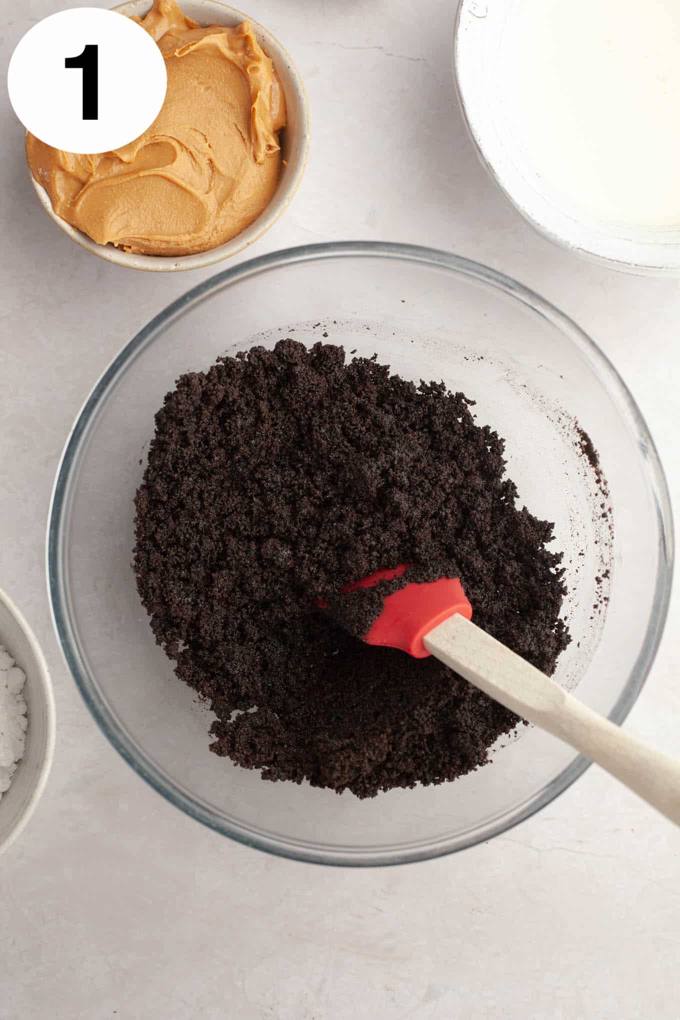 An overhead view of crushed Oreos and butter in a mixing bowl, with a rubber spatula. 