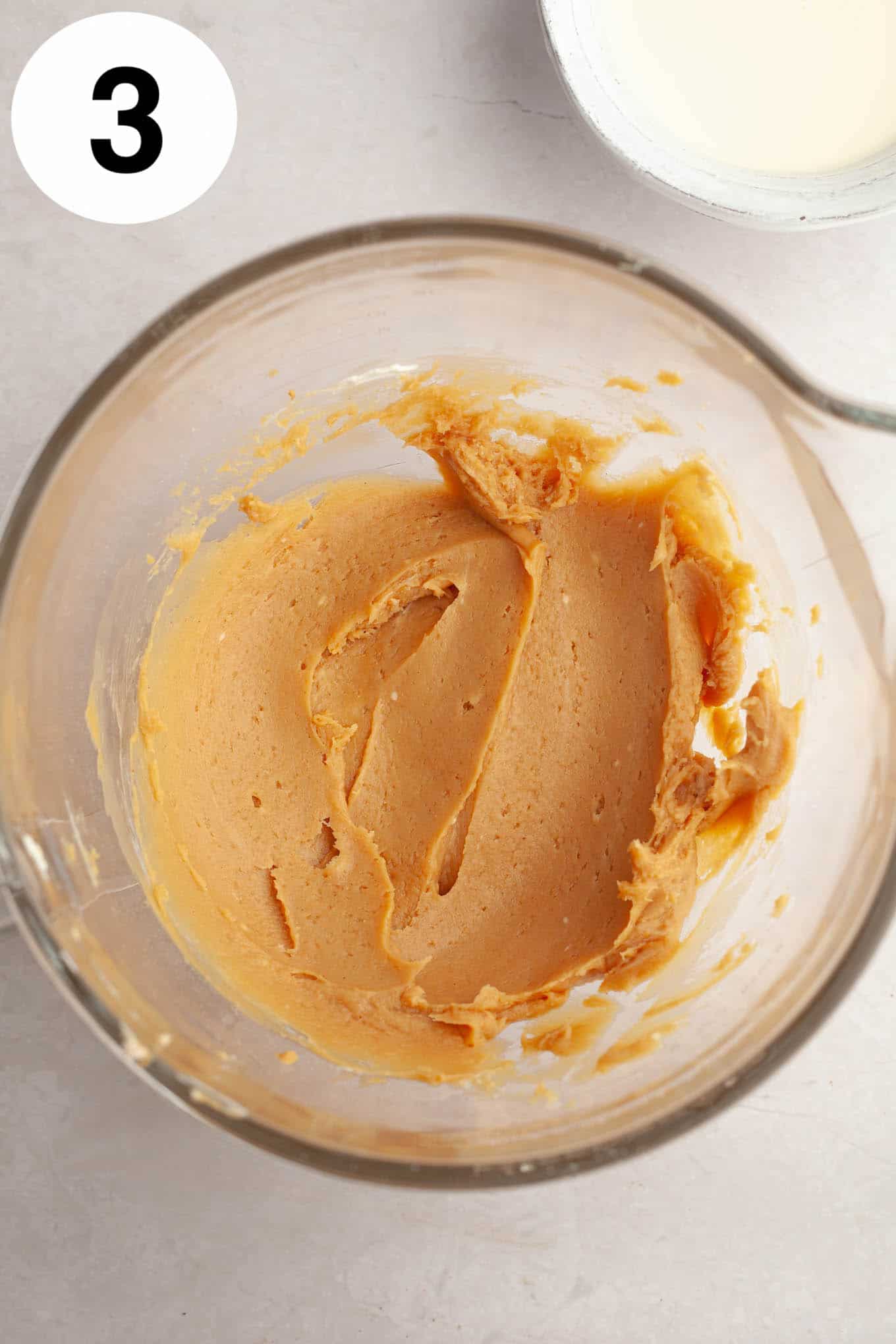 An overhead view of a peanut butter-cream cheese mixture in a glass mixing bowl. 