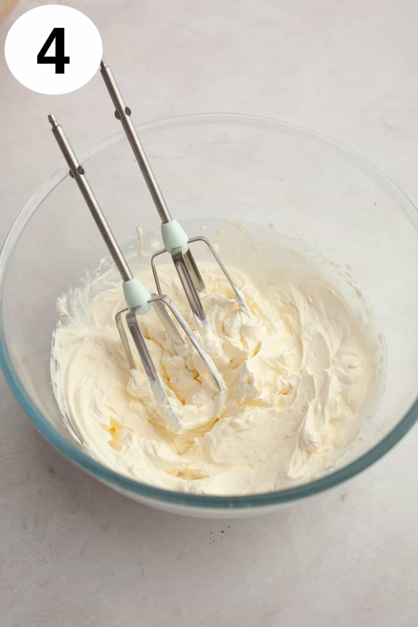 An overhead view of whipped cream in a glass mixing bowl with beaters. 