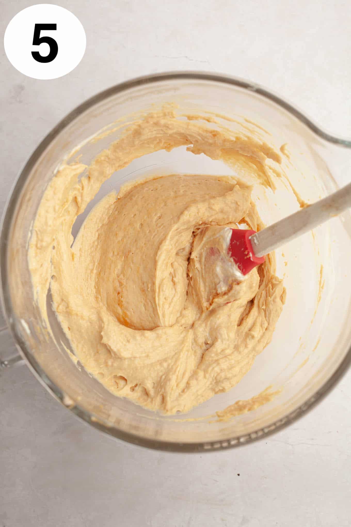 An overhead view of a peanut butter pie filling in a glass mixing bowl. 