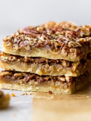 A stack of three pecan pie bars on brown parchment paper.