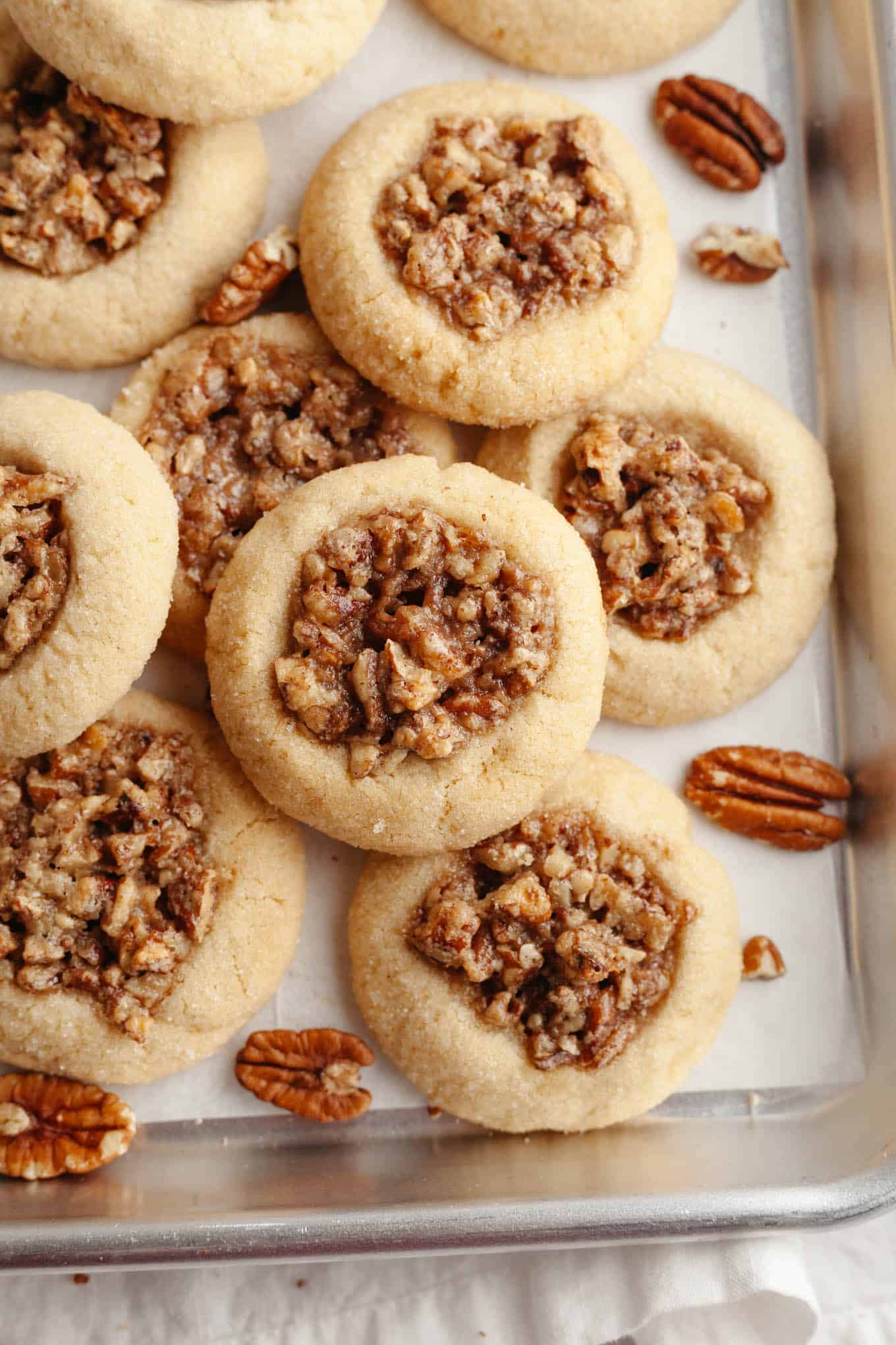 An overhead, close-up view of baked pecan pie cookies on a parchment paper-lined baking sheet. 