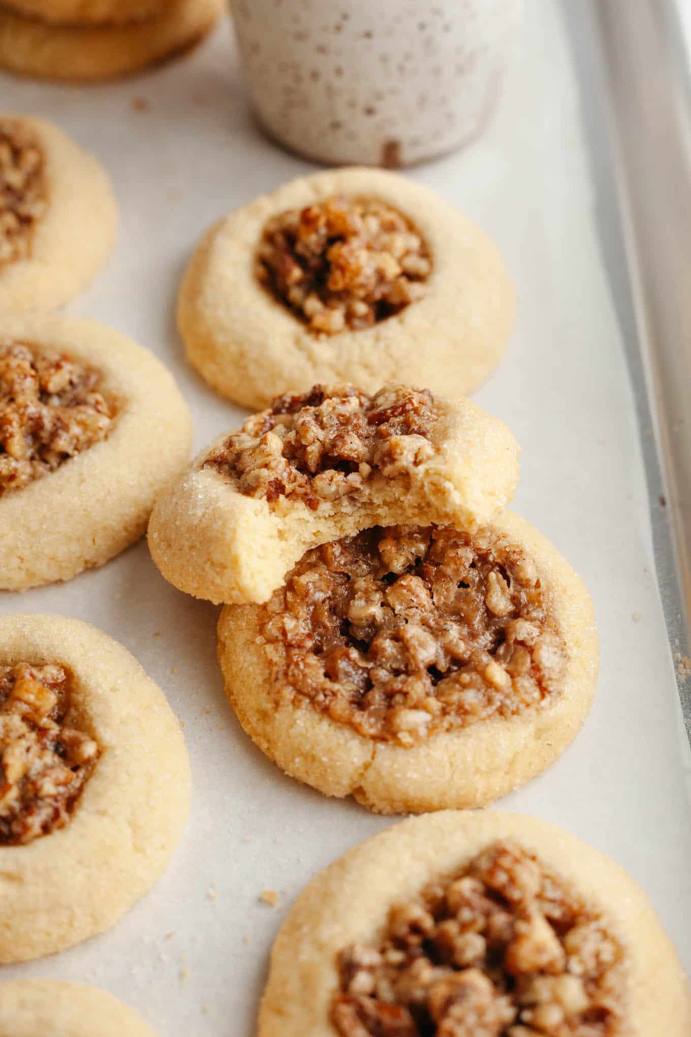 Pecan pie cookies on a parchment-lined baking sheet. One cookie has a bite missing. 