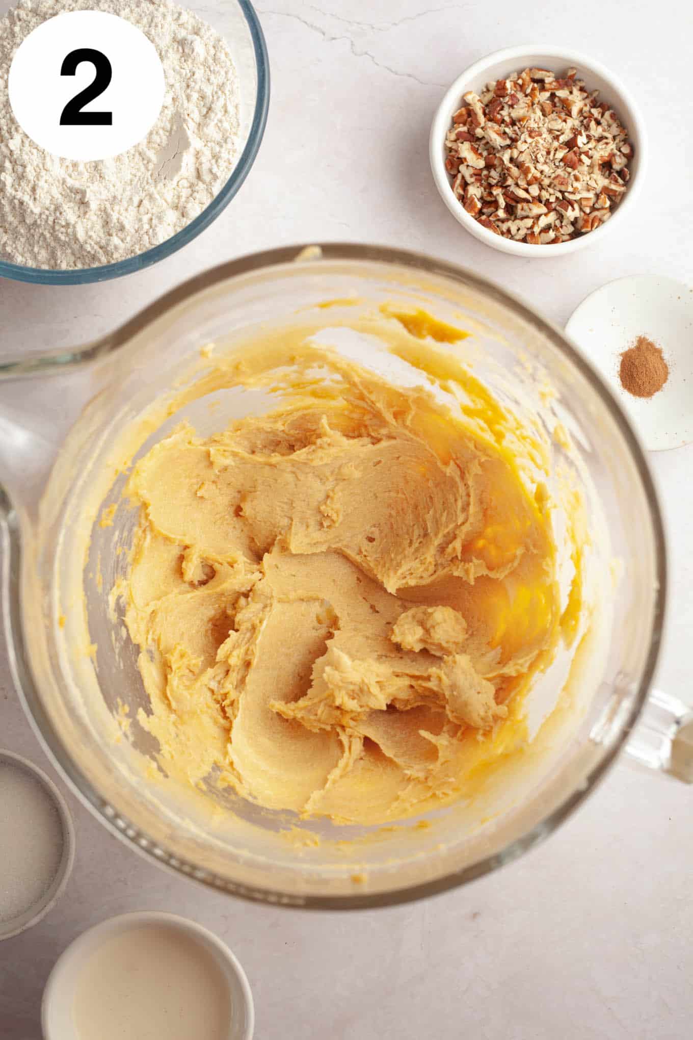 An overhead view of a wet cookie dough mixture in a glass mixing bowl. 