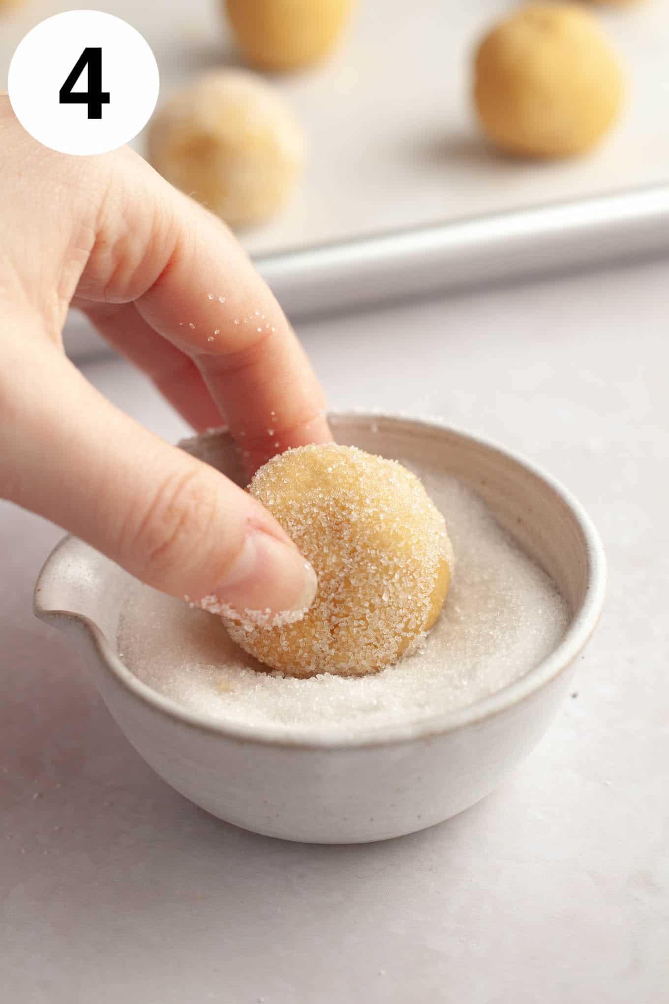 An action shot showing a ball of cookie dough being rolled in sugar. 