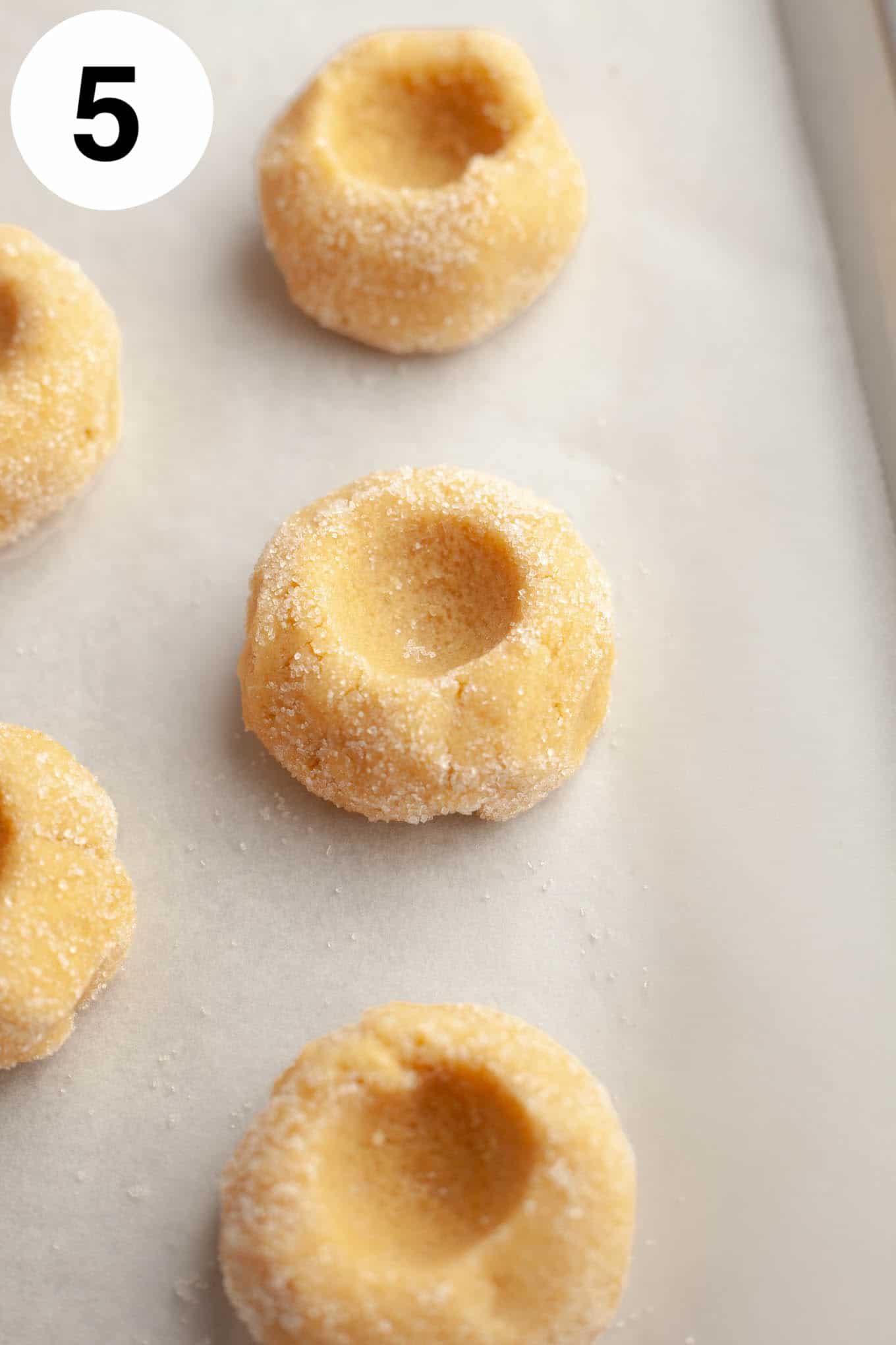Raw, unfilled thumbprint cookies on a parchment paper-lined baking sheet. 