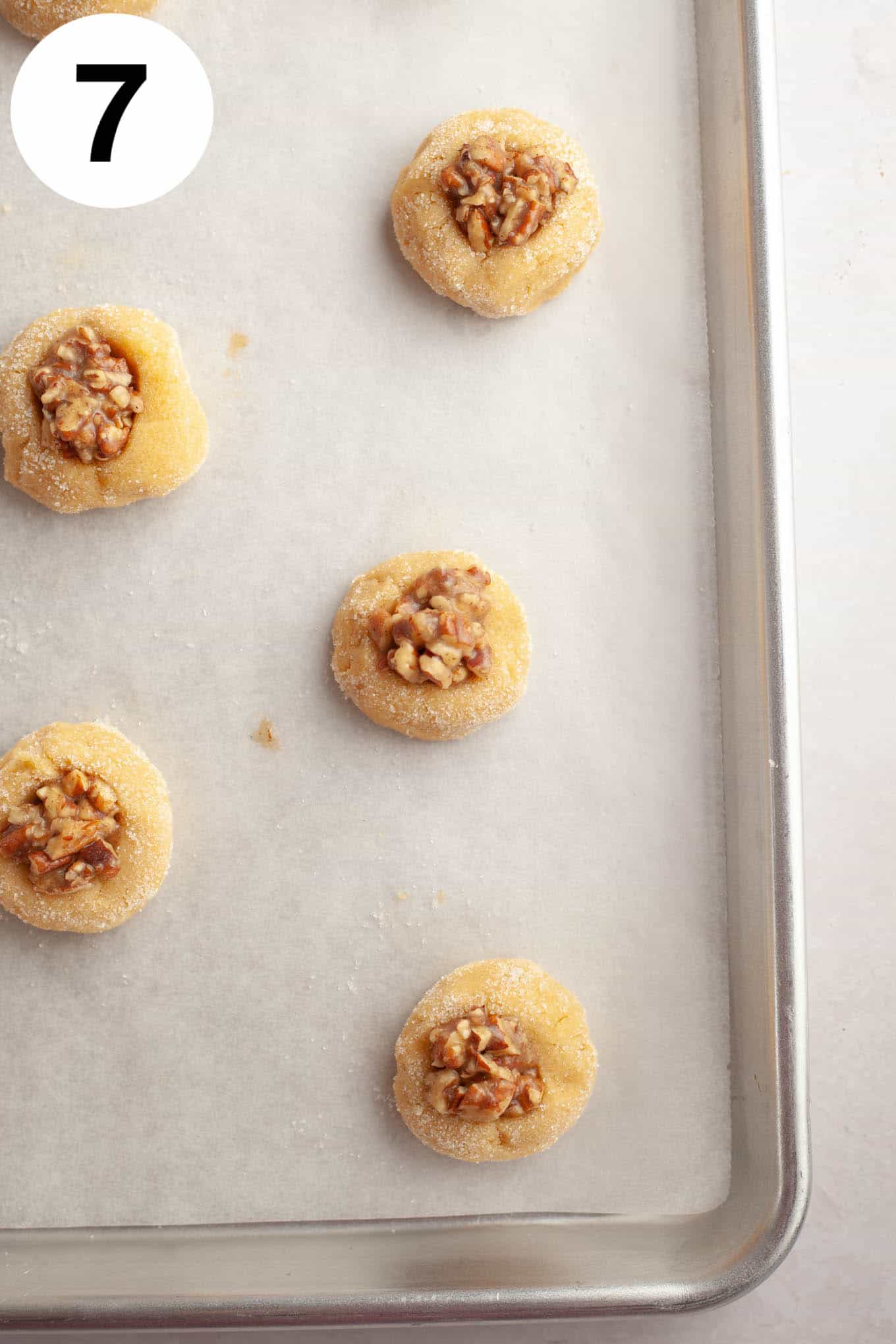 An overhead view of unbaked pecan pie cookies on a parchment paper-lined baking sheet. 