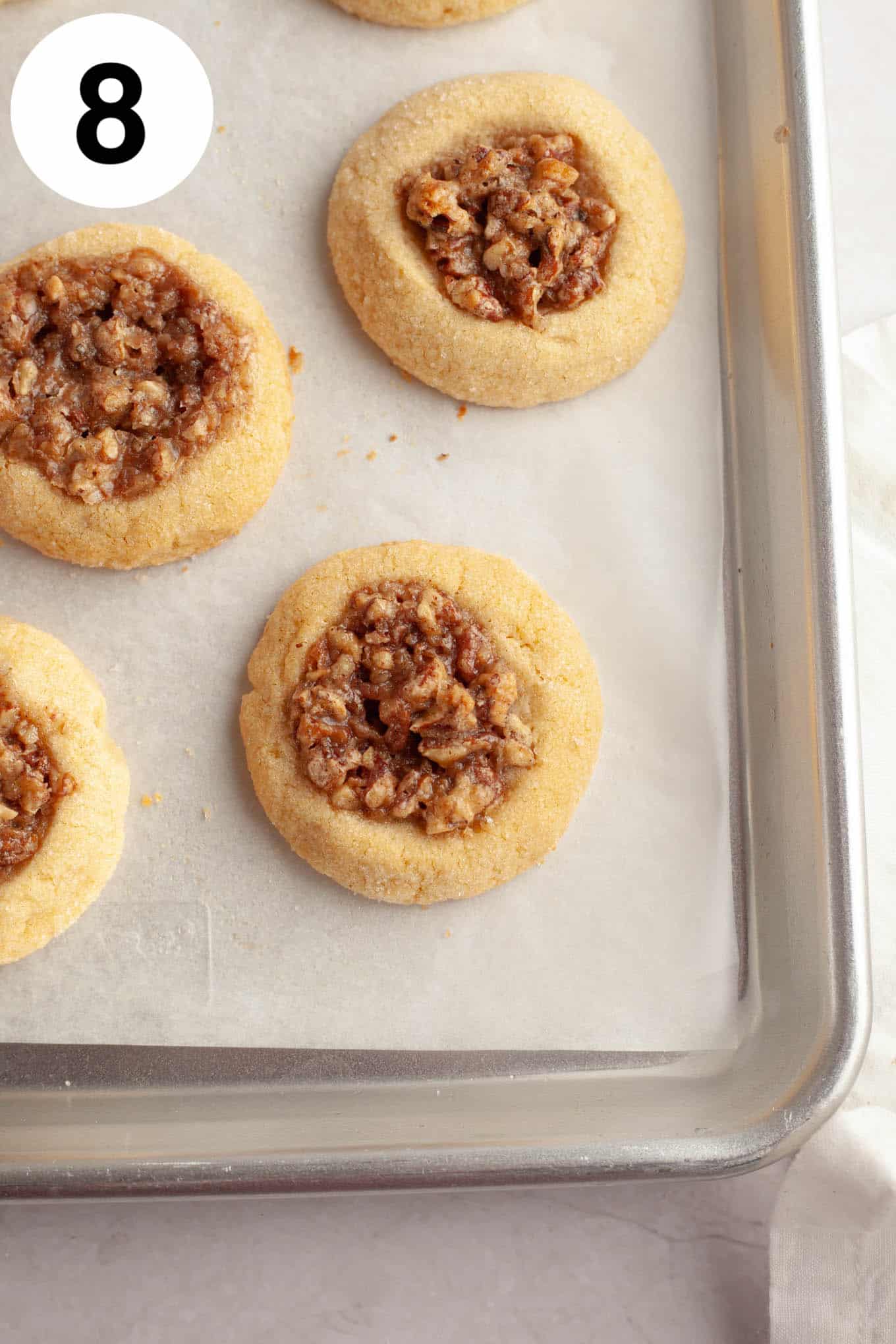 An overhead view of baked pecan pie cookies on a parchment paper-lined baking sheet. 