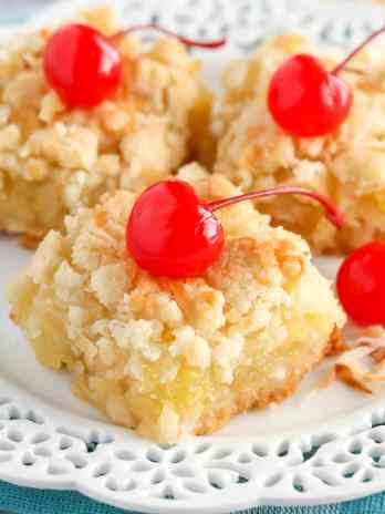 Three pineapple bars garnished with maraschino cherries on a white dessert plate.