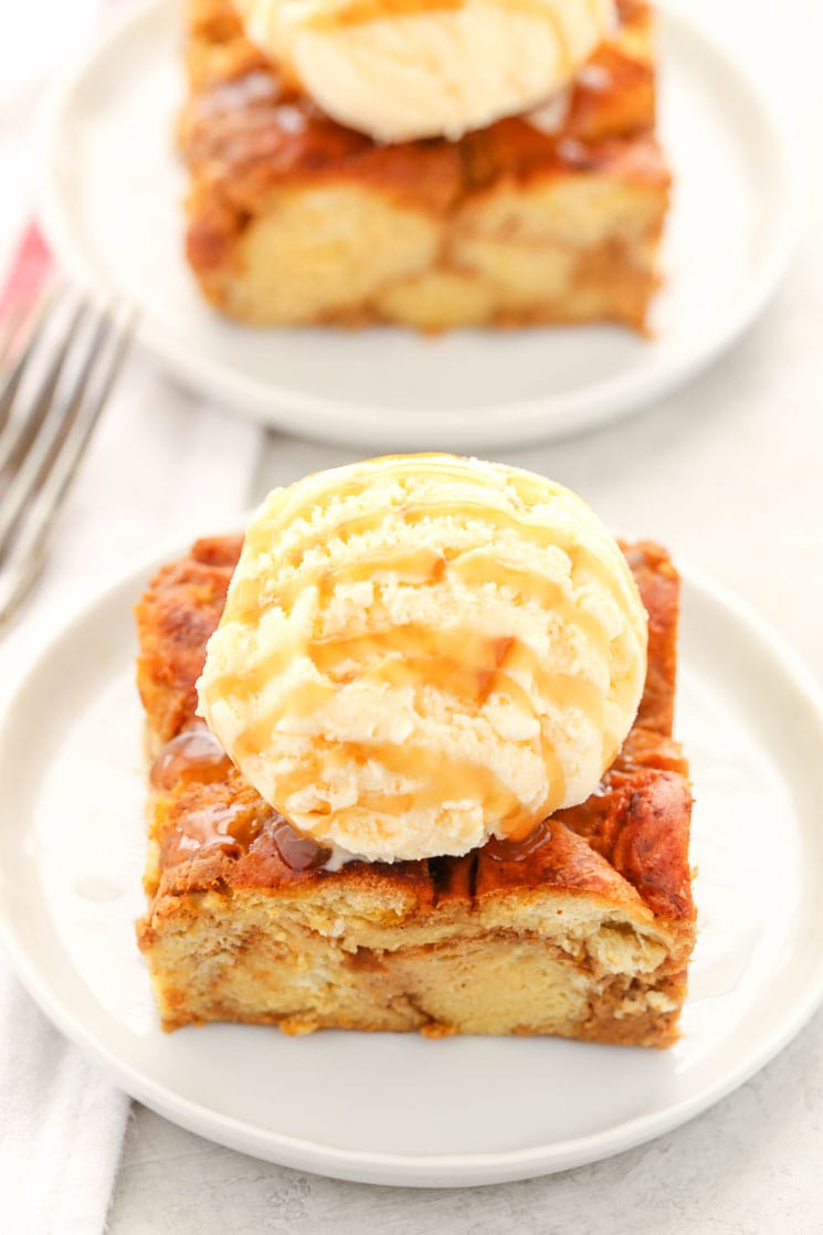 Two slices of pumpkin bread pudding topped with ice cream and caramel sauce on white plates. 