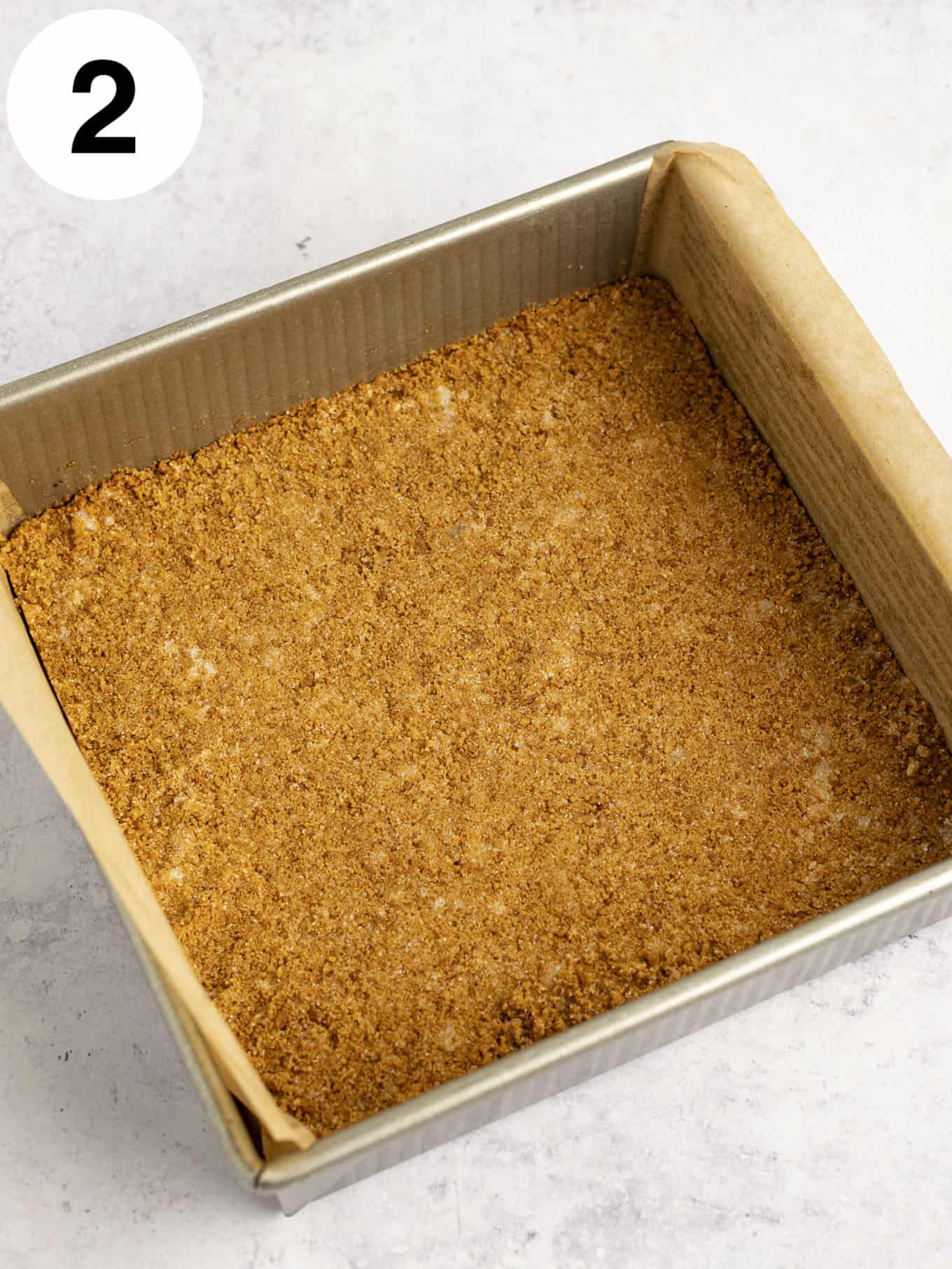 An overhead view of a gingersnap crust pressed into a 9-inch square pan. 