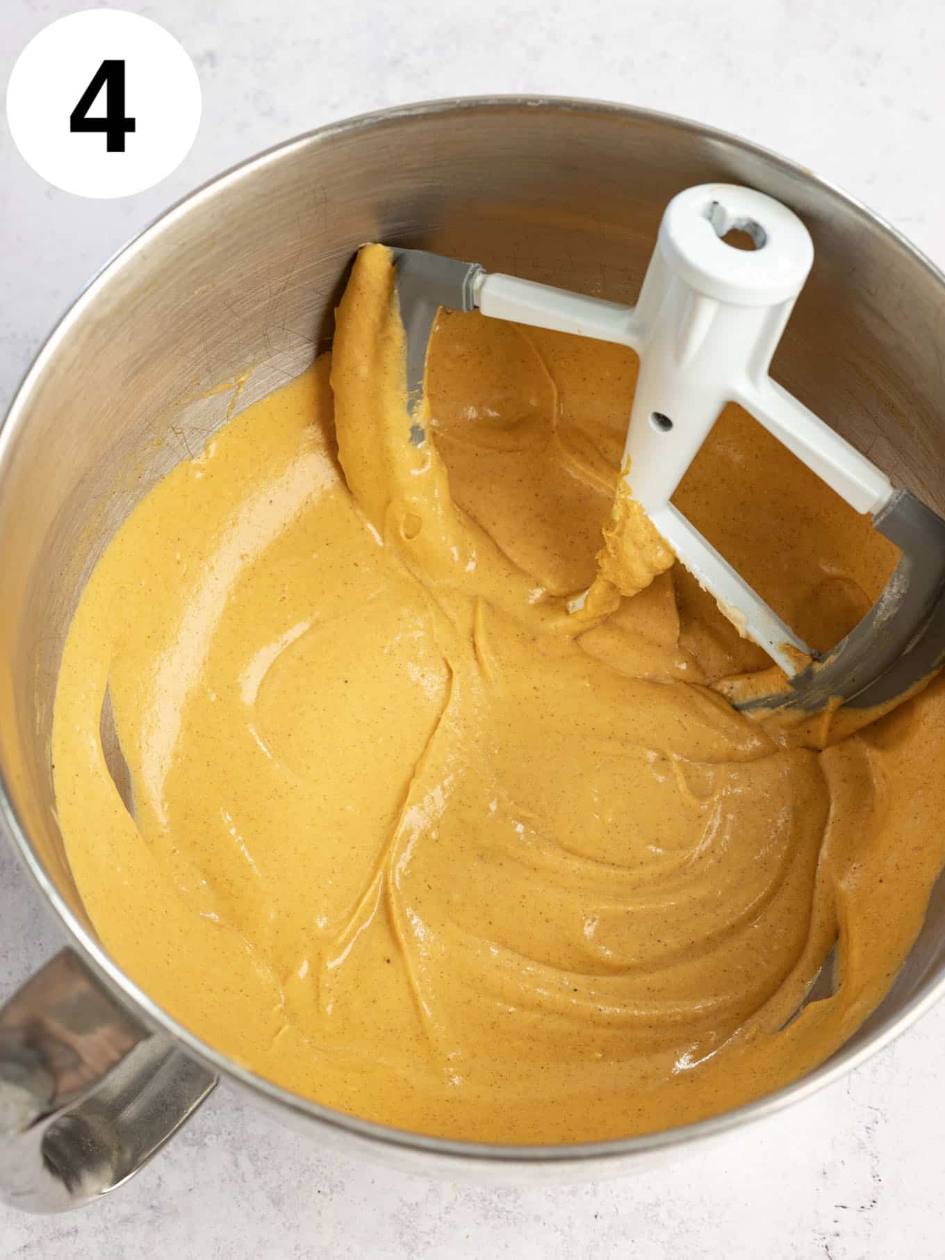 An overhead view of pumpkin cheesecake filling in the bowl of a stand mixer, with a paddle attachment. 