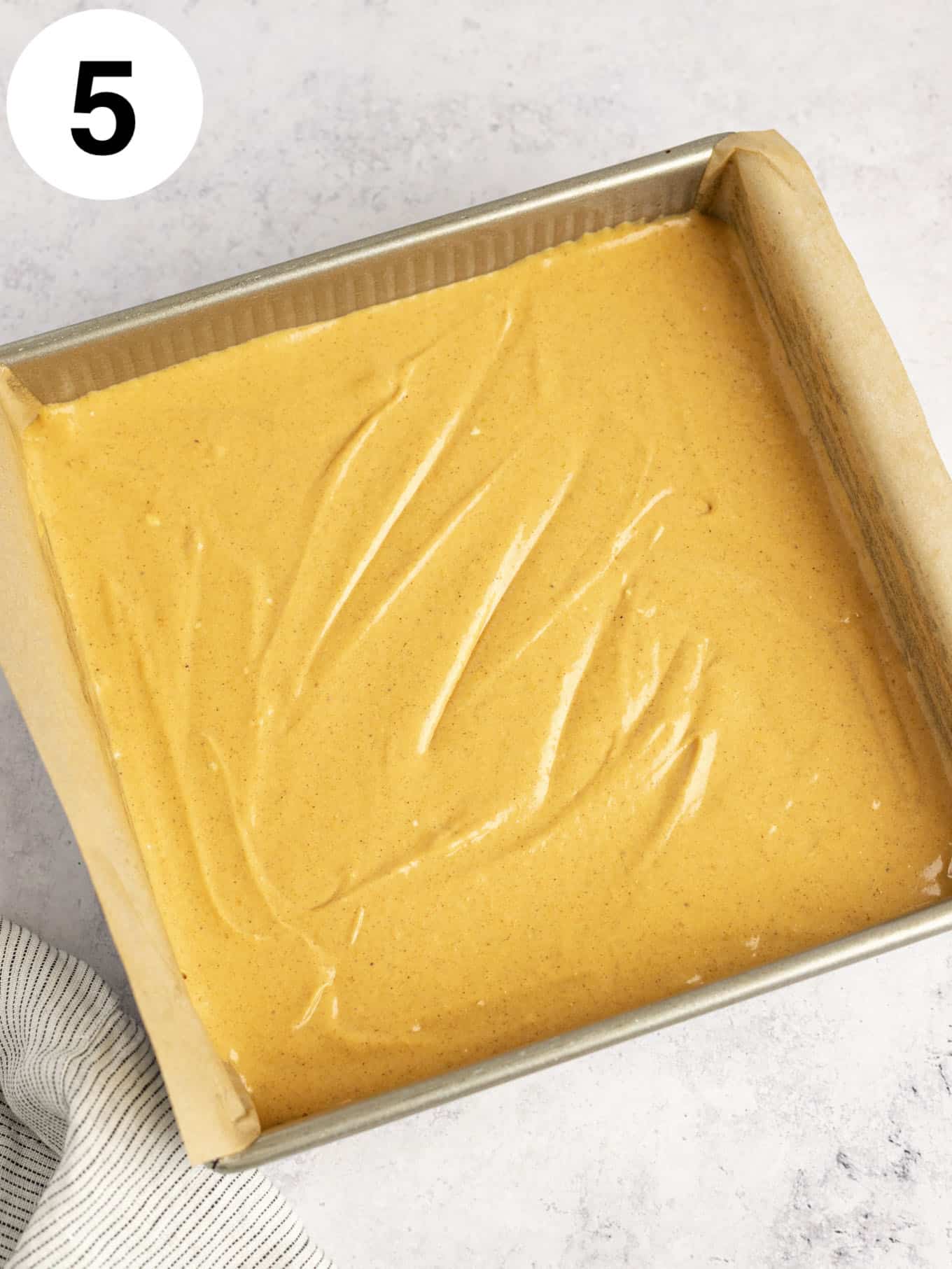 An overhead view of unbaked pumpkin cheesecake bars in a lined baking dish. 