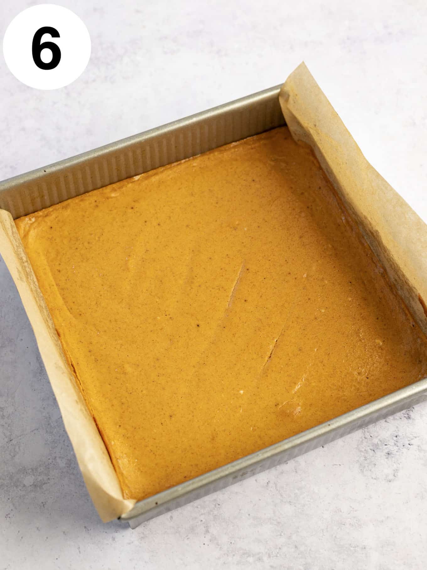 An overhead view of baked pumpkin cheesecake bars in a lined baking dish. 