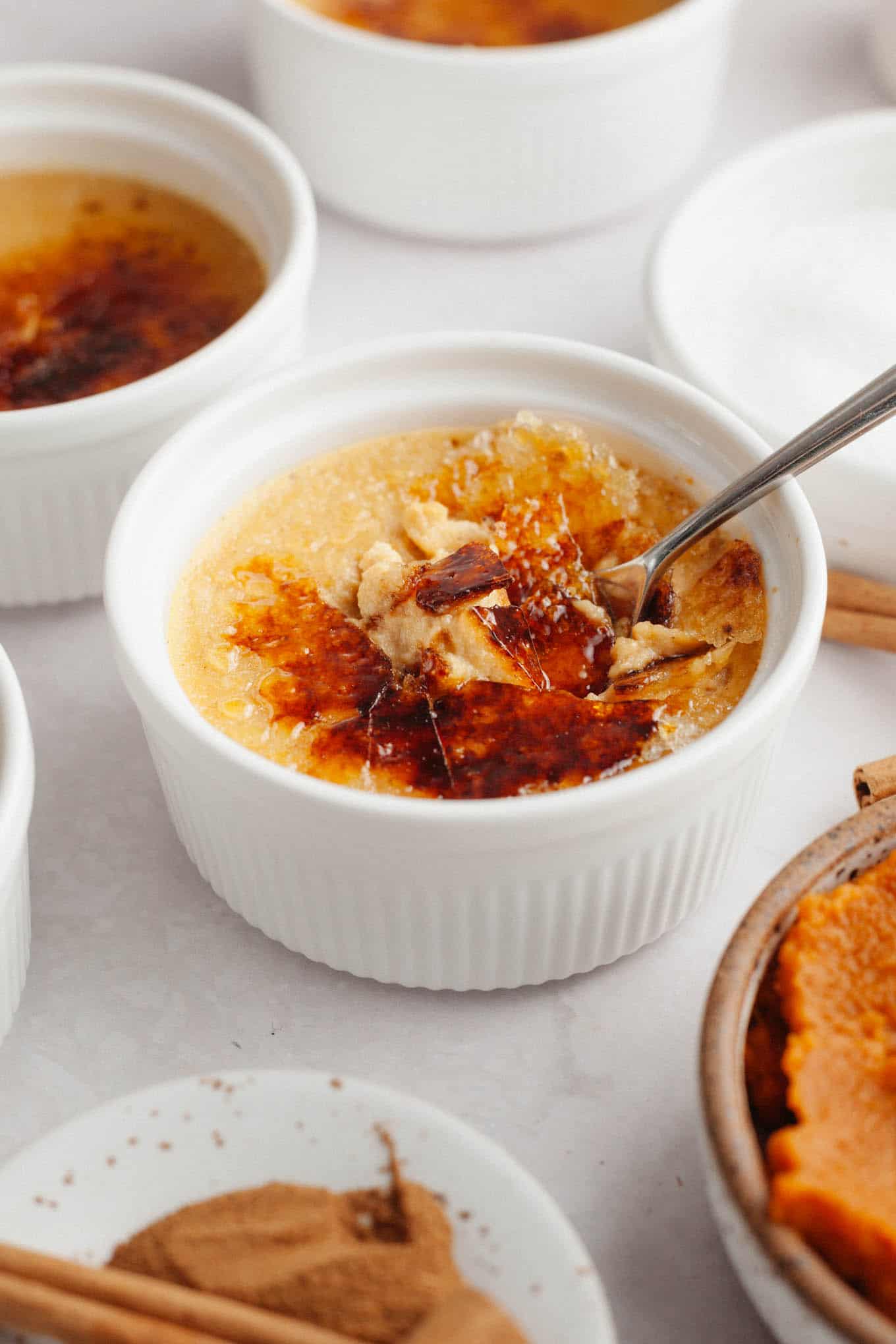 A ramekin of pumpkin crème brûlée, with the caramelized sugar topping cracked open with a spoon. 