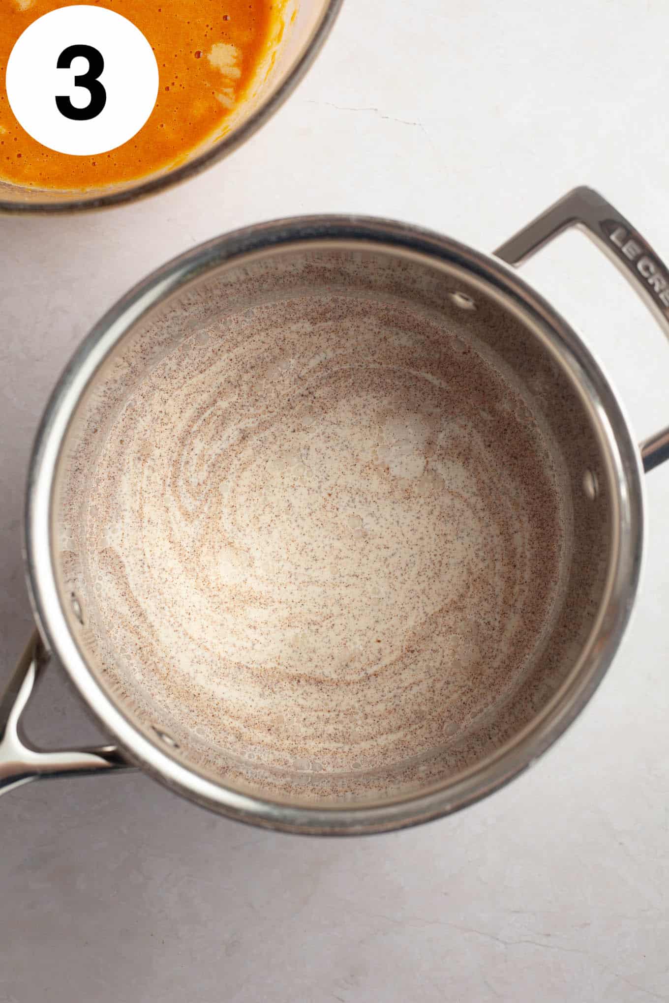 An overhead view of heavy cream and pumpkin spice in a saucepan. 