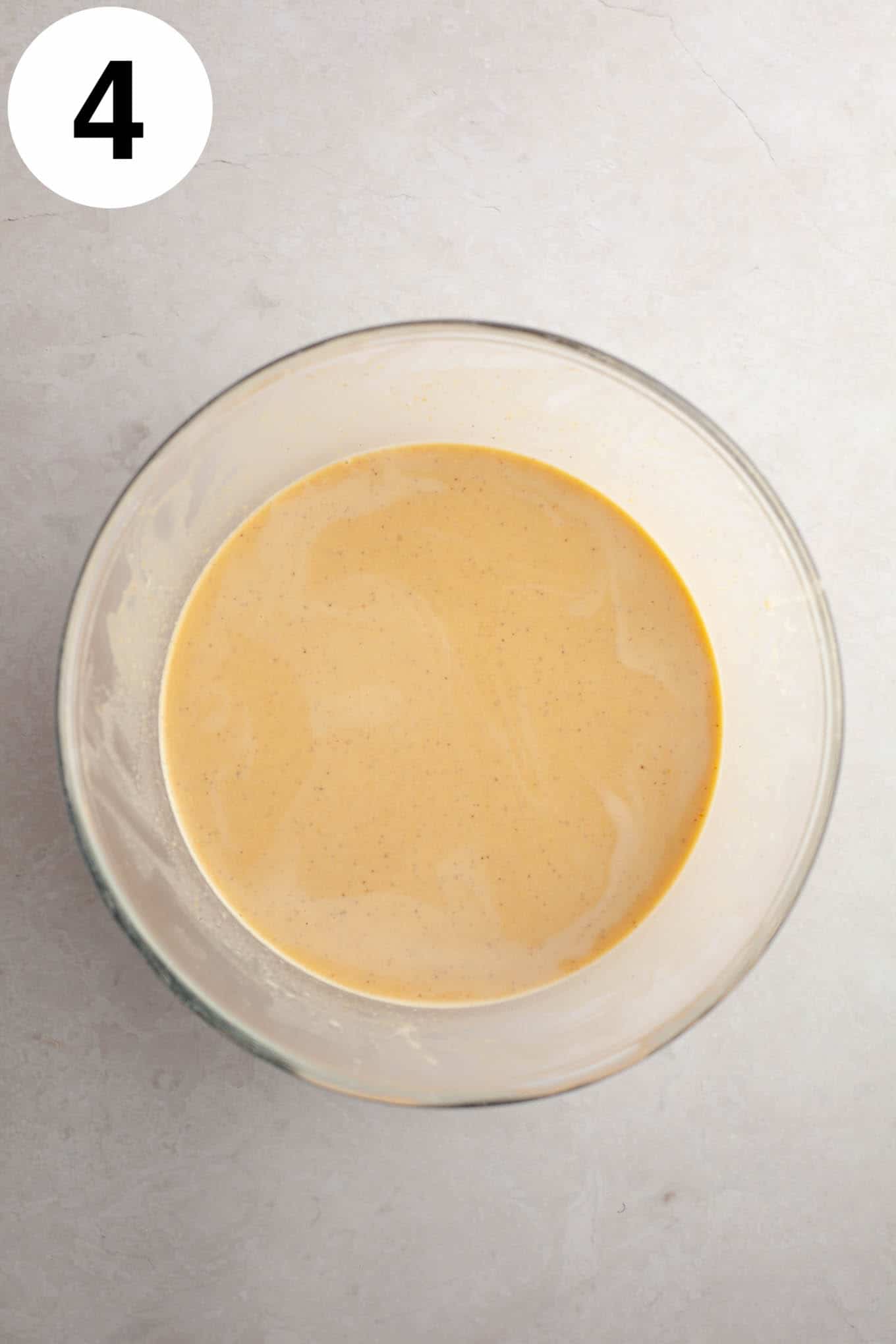 An overhead view of raw pumpkin crème brûlée filling in a glass mixing bowl. 