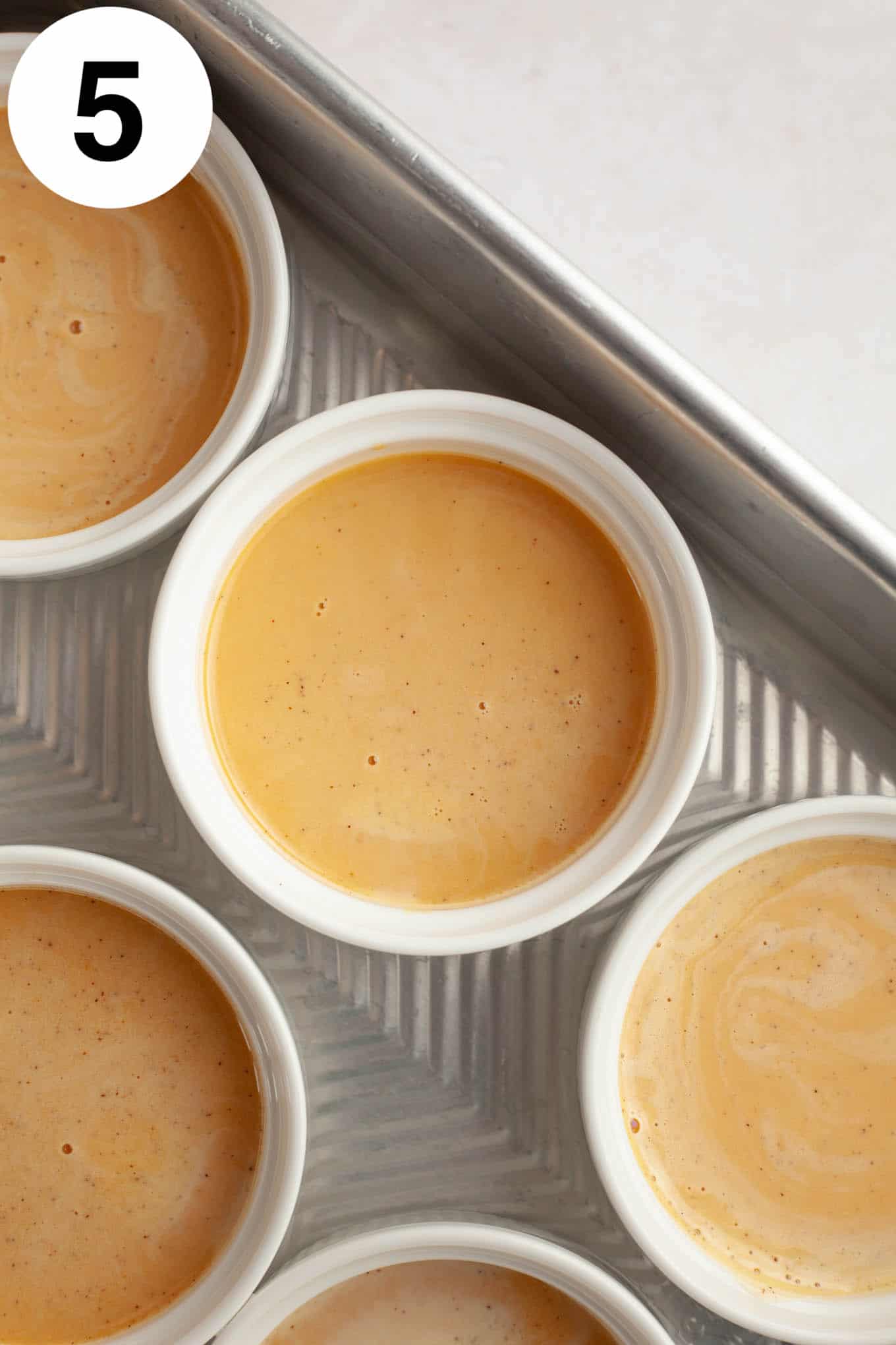 An overhead view of unbaked pumpkin crème brûlée in individual ramekins. 