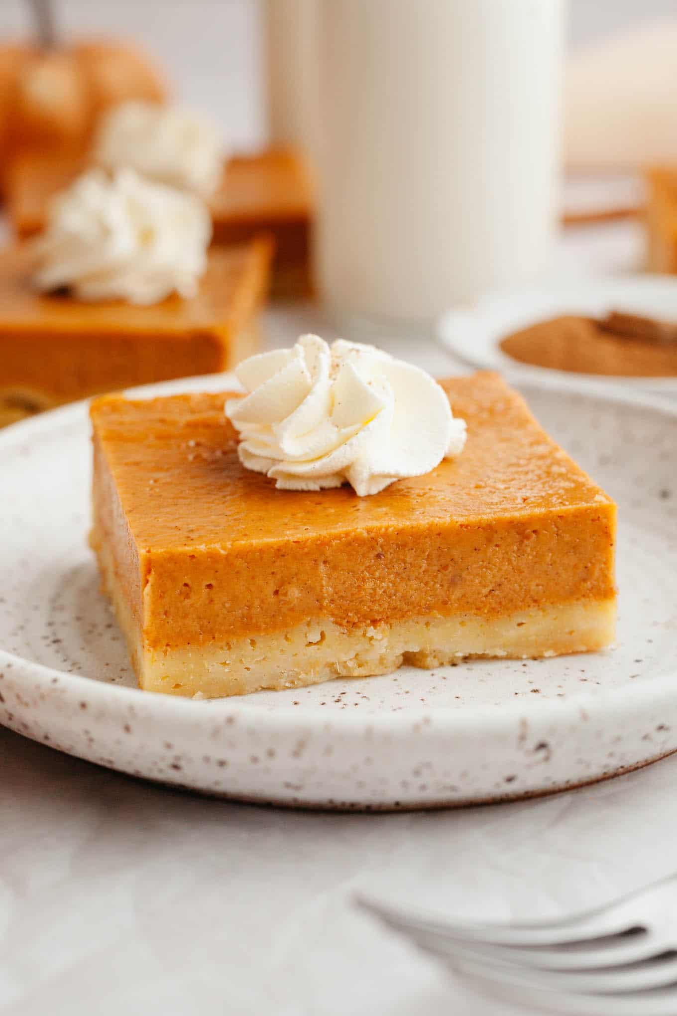 A pumpkin pie bar garnished with whipped cream, on a dessert plate. 