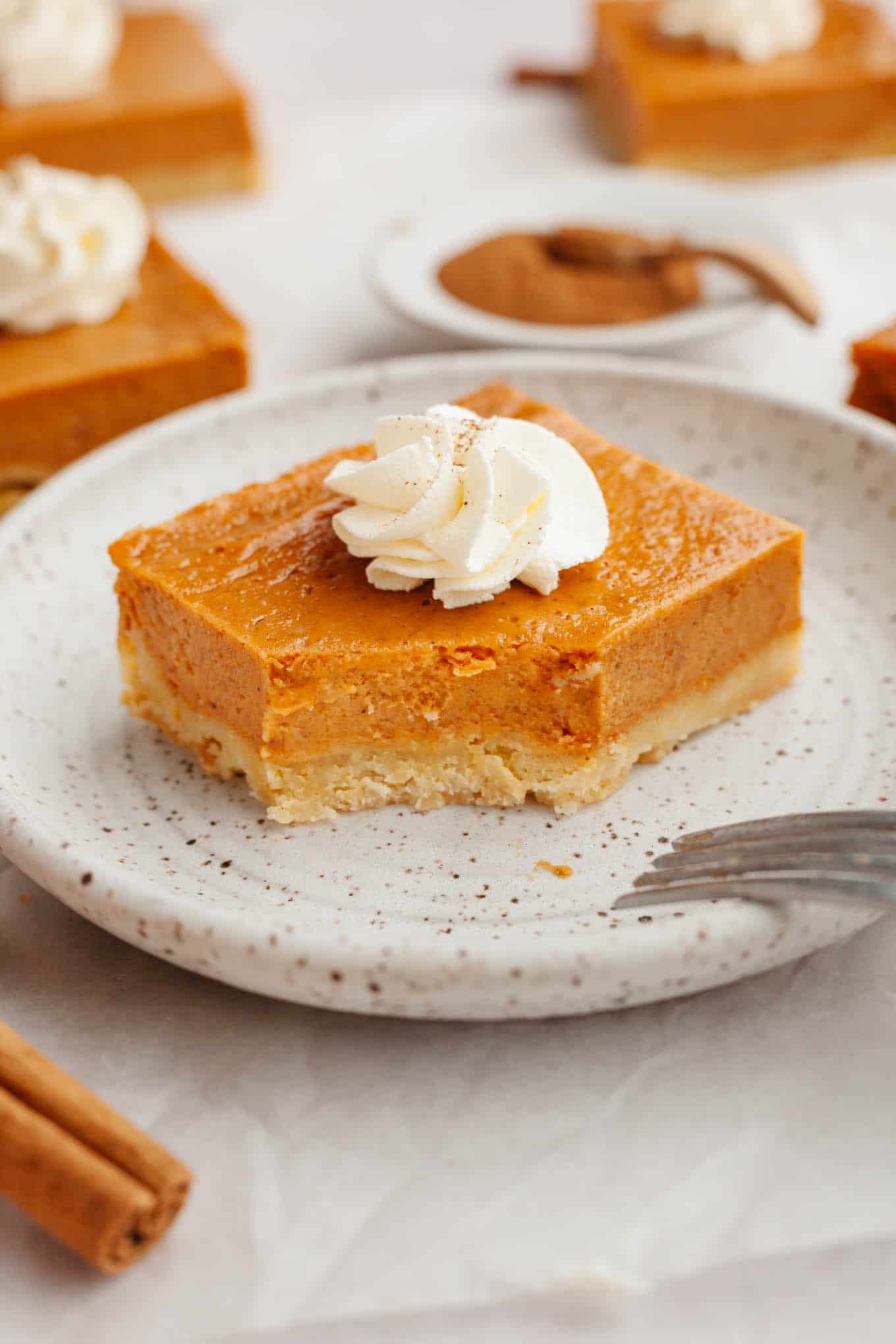A pumpkin pie bar garnished with whipped cream, on a dessert plate. A bite is missing. 